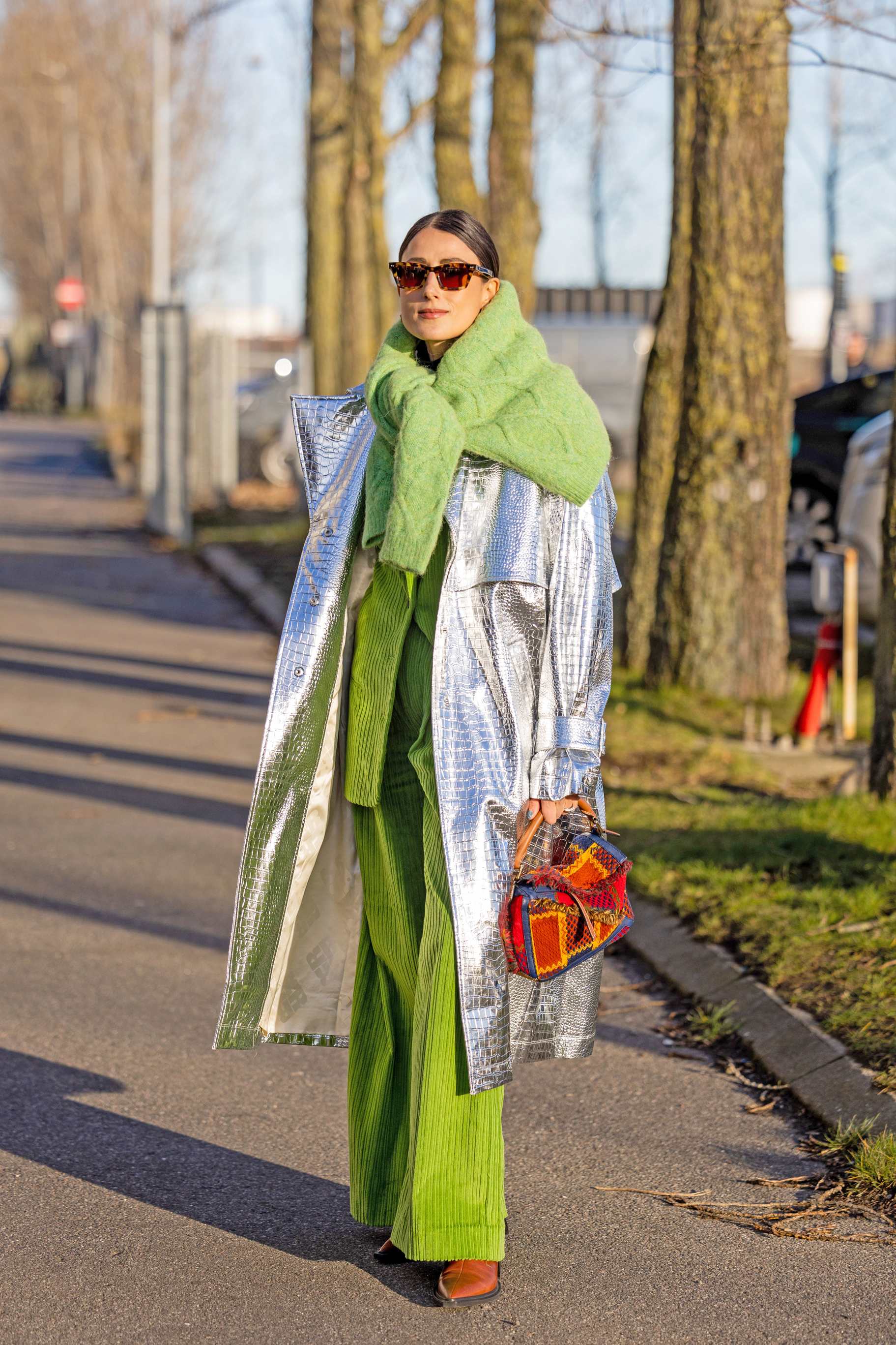 Frau im Copenhagen Streetstyle-Outfit, dänischer Layering-Look mit silbernem Mantel, grünem Dress, Schal und Handtasche, stehend auf Gehweg