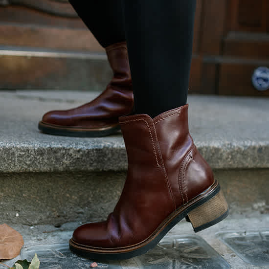 Nahaufnahme dunkelbrauner Leder-Stiefeletten im Dark Academia Style auf Steinboden