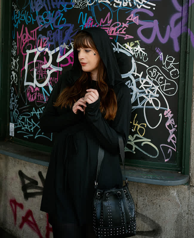 Frau in schwarzem Kapuzenkleid, im Halloween-Look, vor einer Wand mit Graffiti