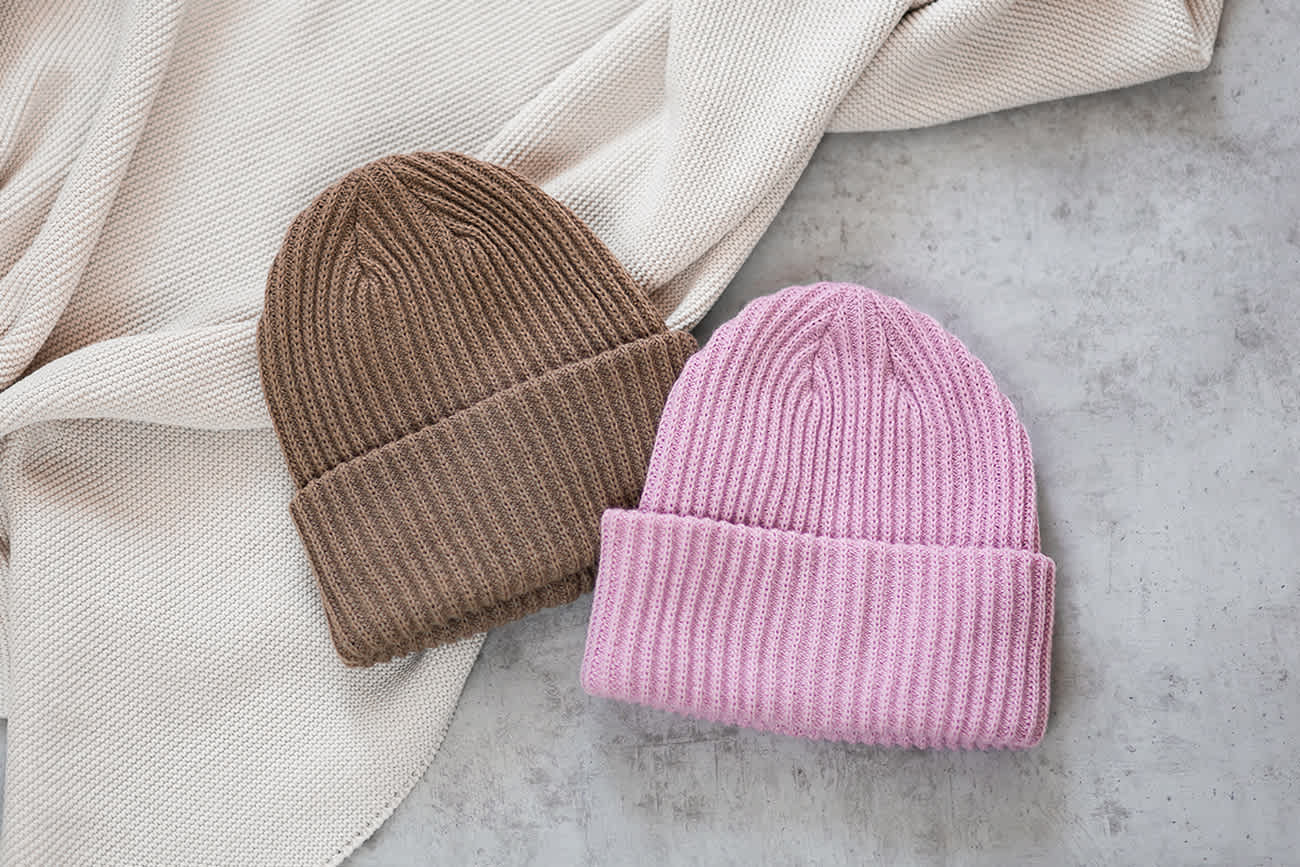 Zwei warme Strickmützen in Braun und Pink, nebeneinander liegend auf einer Decke