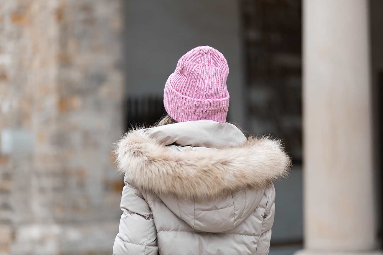 Person mit warmer Winterjacke und Strickmütze in Pink steht mit Rücken zum Betrachter