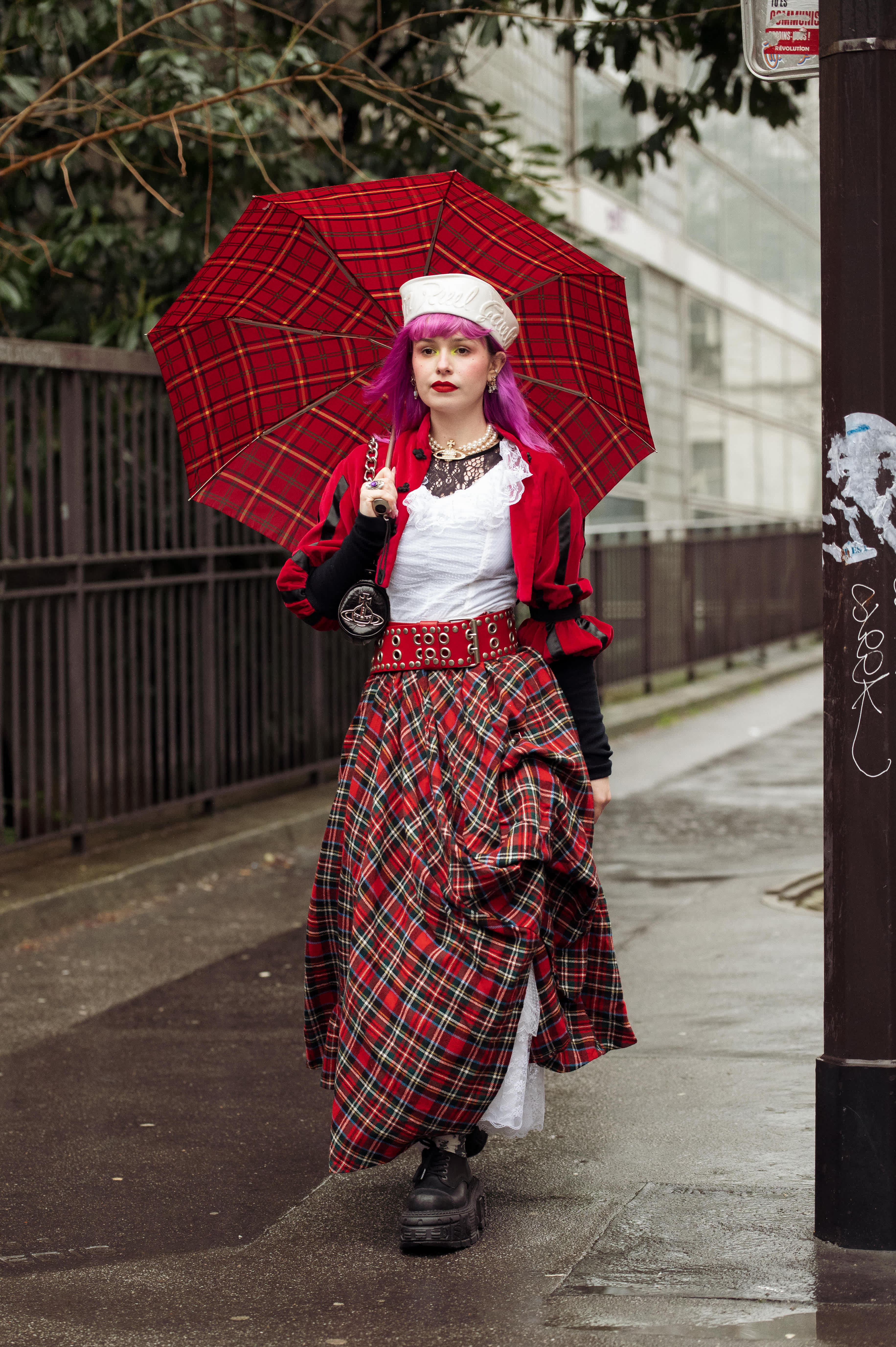 Frau mit langem, roten Schottenrock mit Karomuster samt farblich passendem Regenschirm im Punk-Look