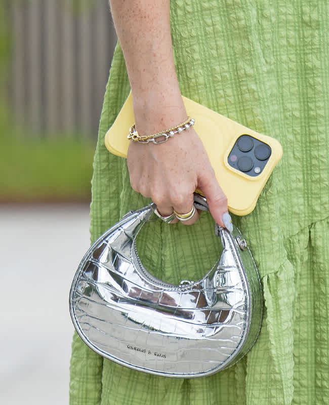 Person hält Handtasche mit Metallic-Finish, gemeinsam mit Handy in Hand, Nahaufnahme