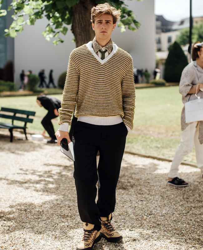 Mann mit gestreiftem Sweater, schwarzer Hose und Retro Sneakern steht auf Kiesweg