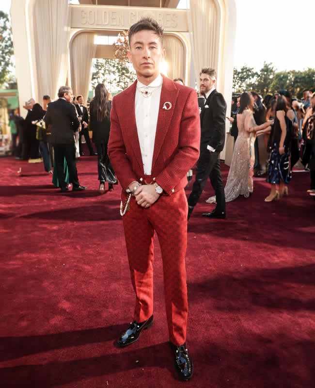 Barry Keoghan in rotem Anzug mit weißem Hemd und Accessoires, posierend auf dem roten Teppich bei einer Veranstaltung.