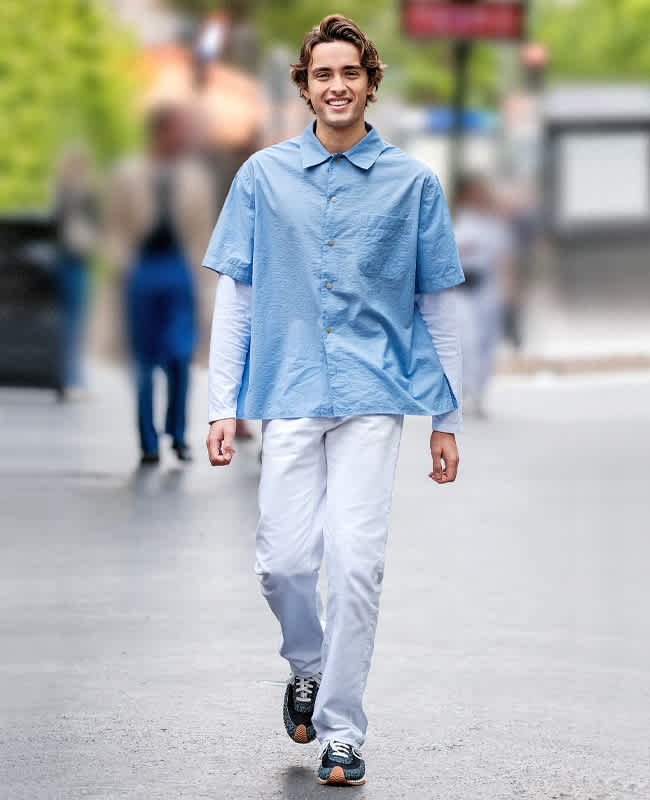 Mann in Casual Outfit mit blauem Hemd, Sneakern und weißer Hose, geht in Richtung Kamera