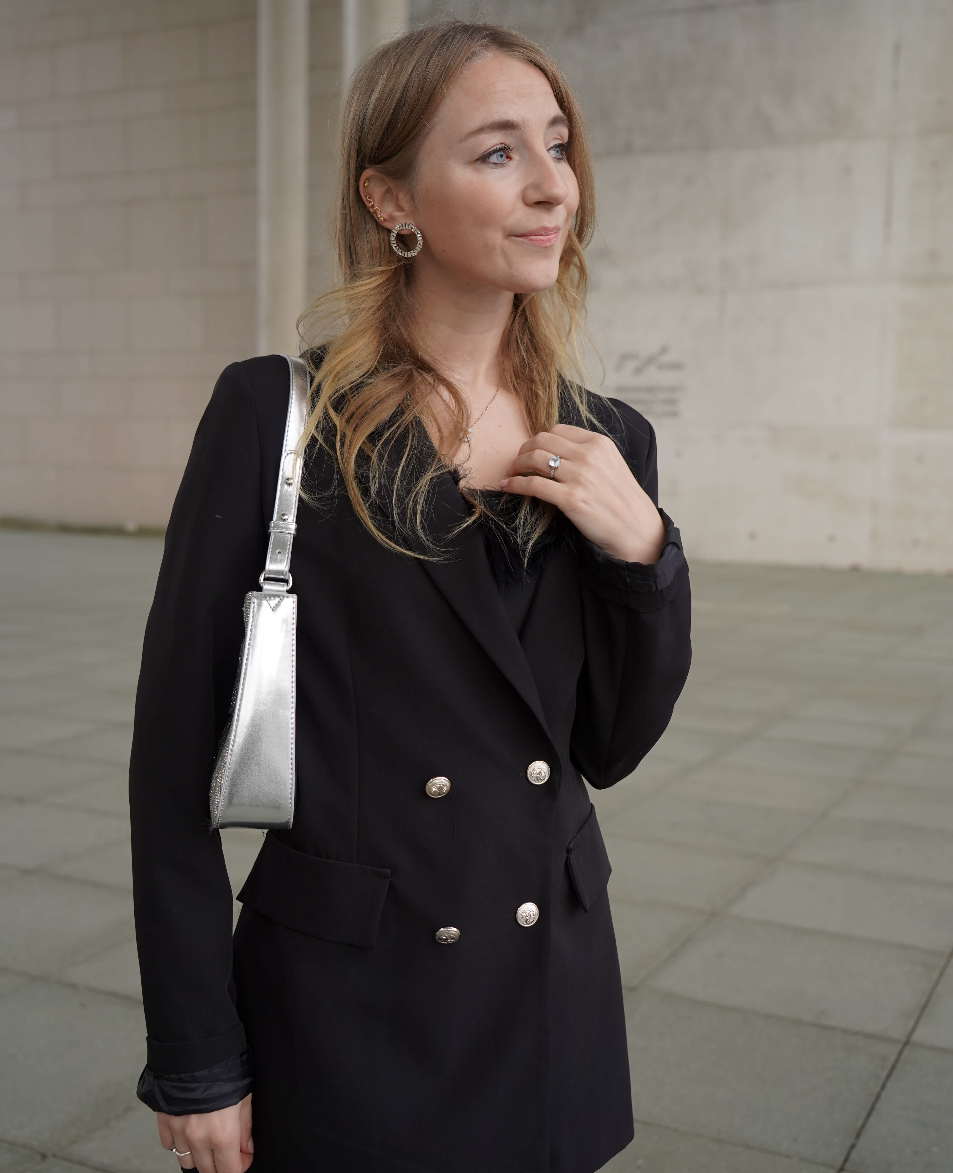 Frau in edlem Blazer-Dress in Schwarz trägt silberne Clutch und glitzernde Creolen-Ohrringe