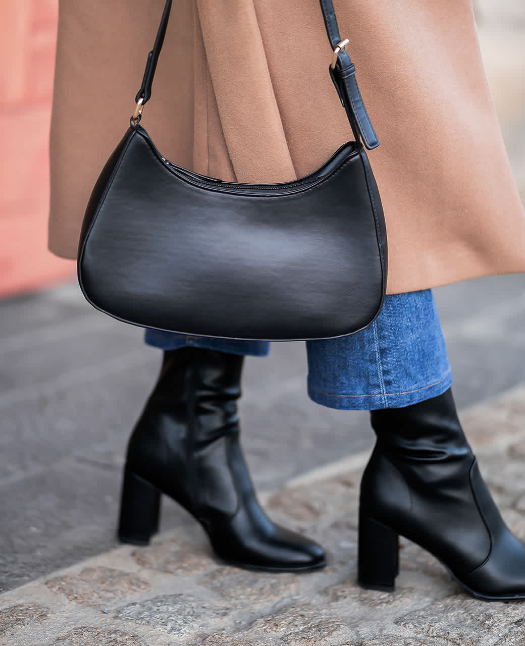 Close-Up einer Frau, die schwarze Stiefeletten mit blauer Jeanshose und schwarzer Handtasche kombiniert