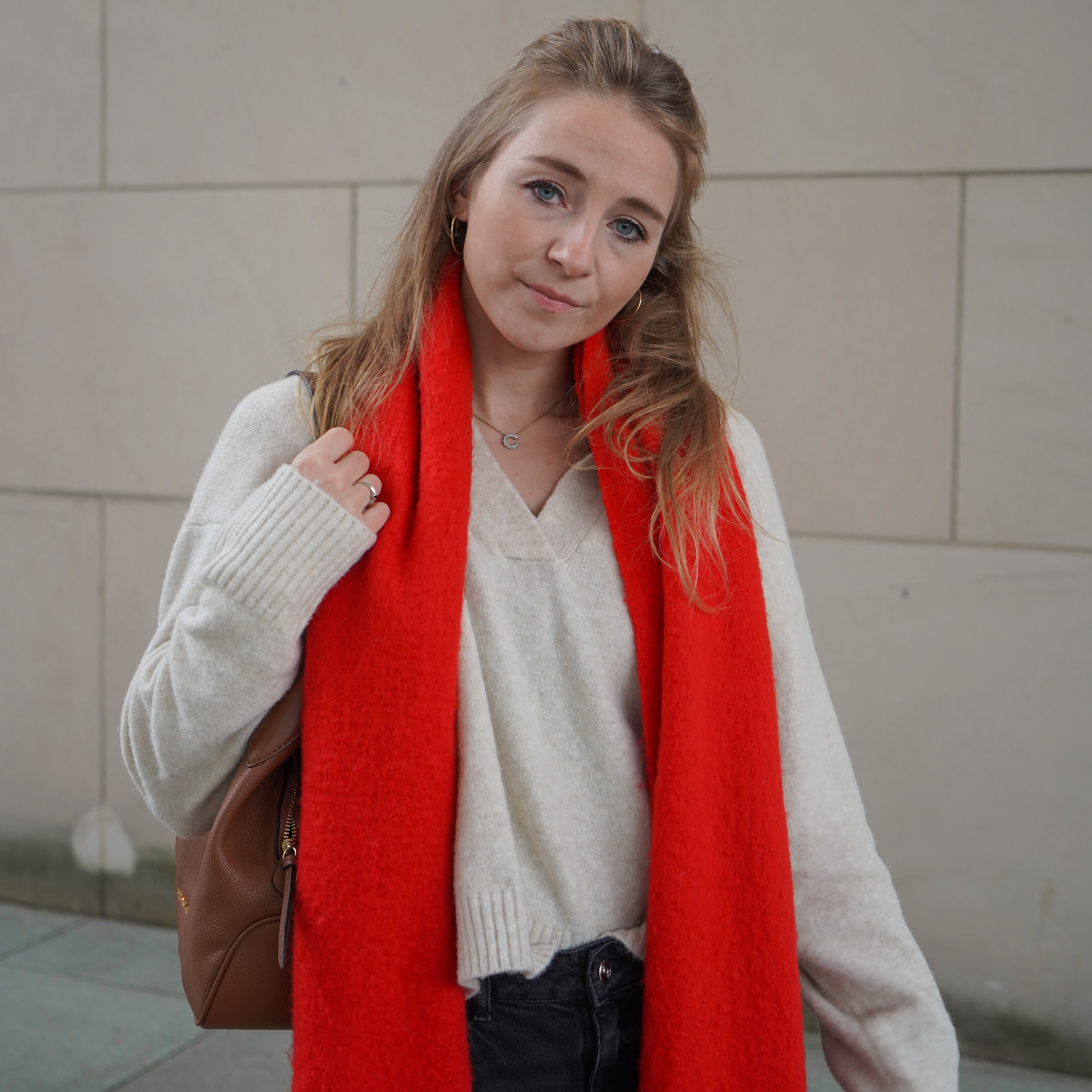 Frau trägt weißen Strickpullover und roten Schal, lässig um den Hals liegend für einen Cozy Style, in Kombination mit brauner Tasche.