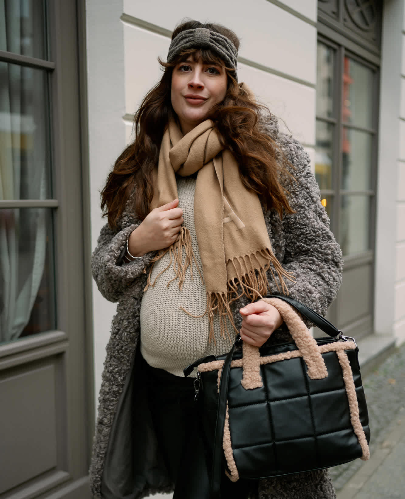 Frau in gemütlich warmer Kleidung mit Mantel, Schal, Strickpullover und Handtasche