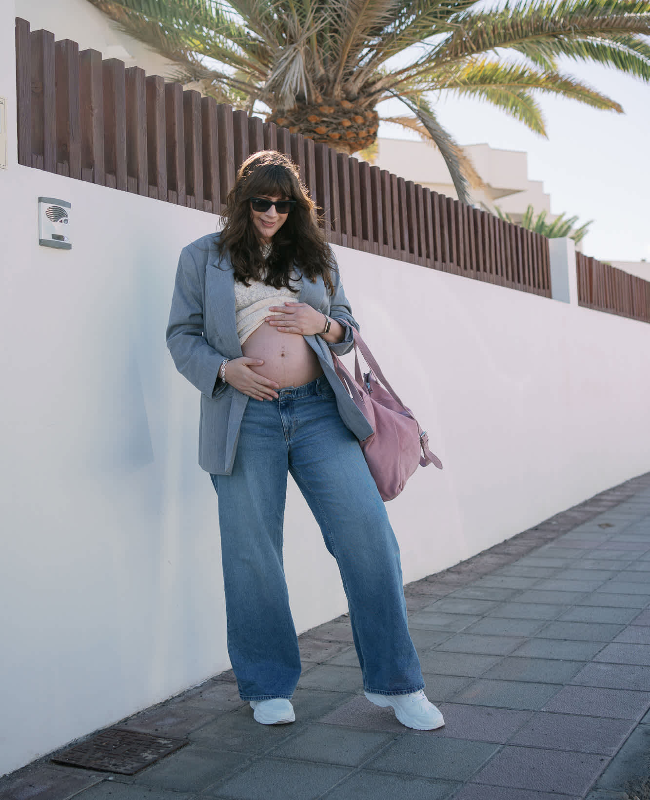 Frau in blauem Jeans-Outfit hält sich Babybauch