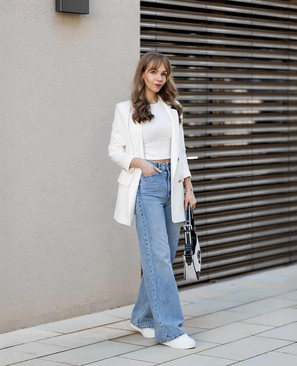 Frau mit Oversized-Blazer, blauen Wide Leg Jeans und weißen Sneakern der Marke Bench