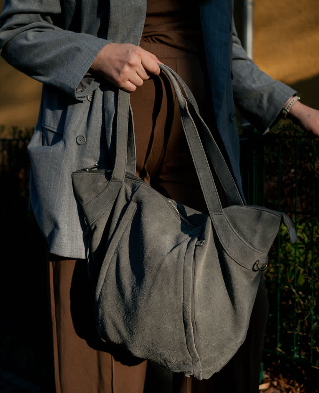 Nahaufnahme einer Frau mit braunem Outfit und graum Blazer, graue Tascher in ihrer Hand
