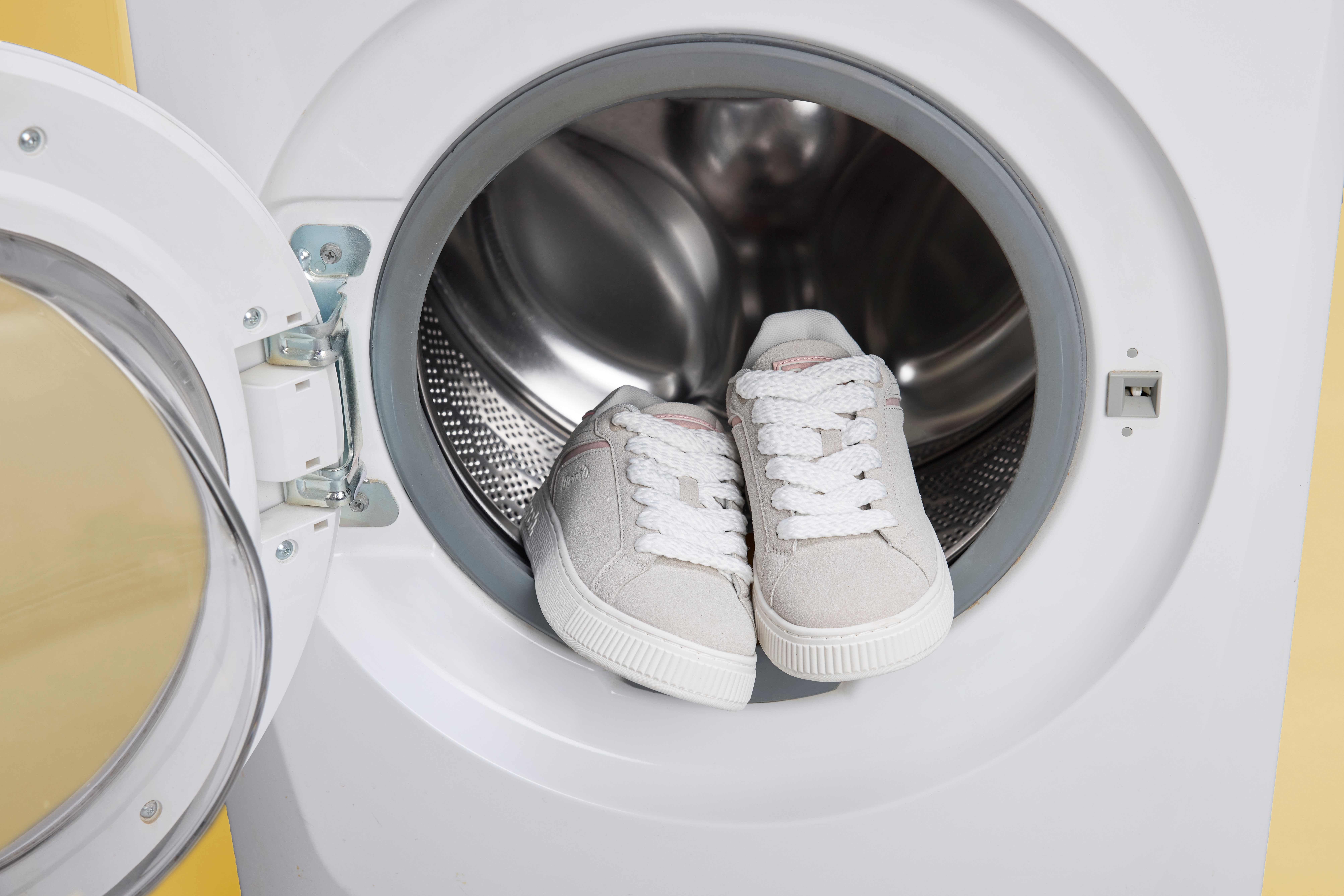 Weiße Schuhe stehen in offener Waschmaschine, bereit für den Waschgang