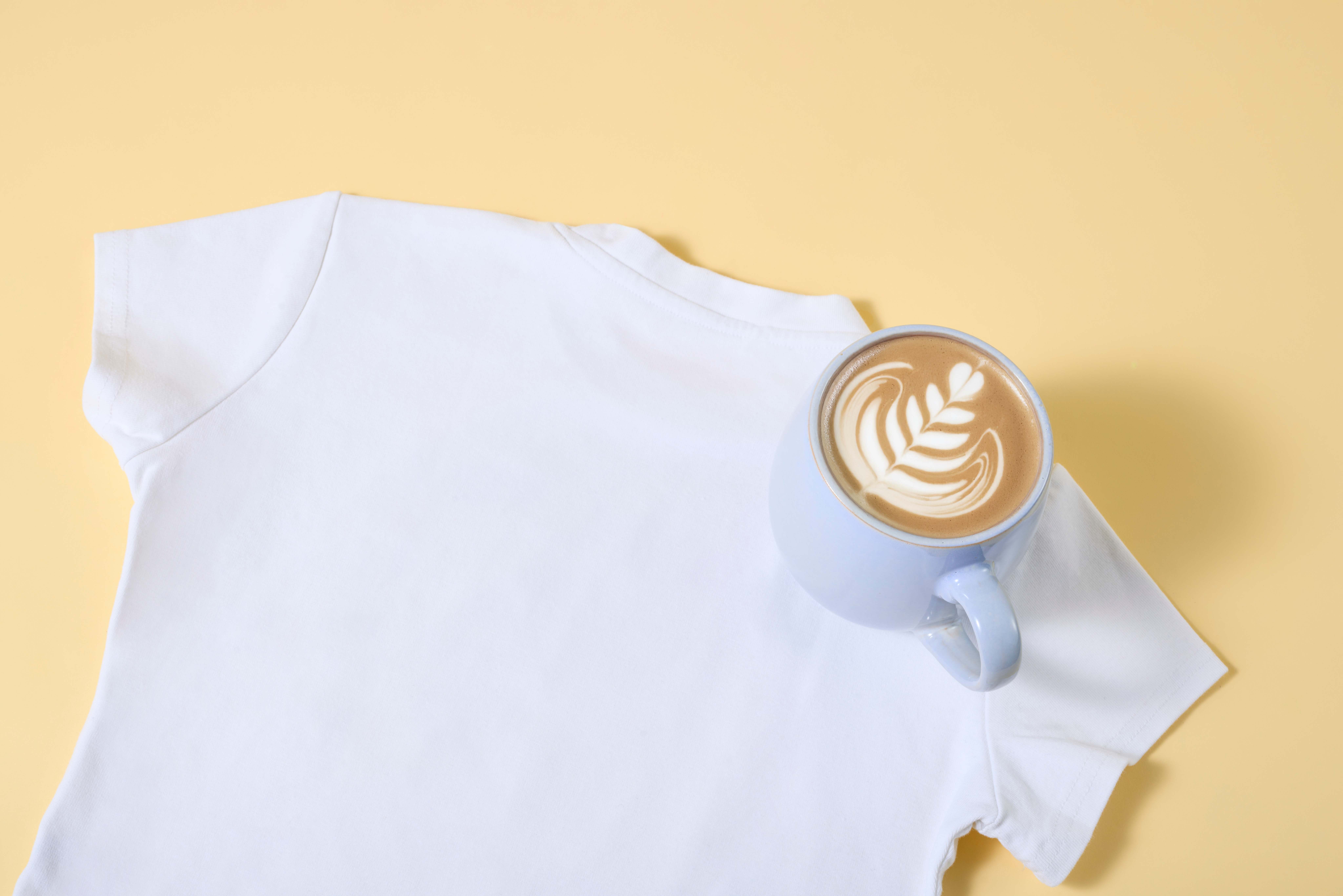 Tasse mit Kaffee steht auf weißem Shirt