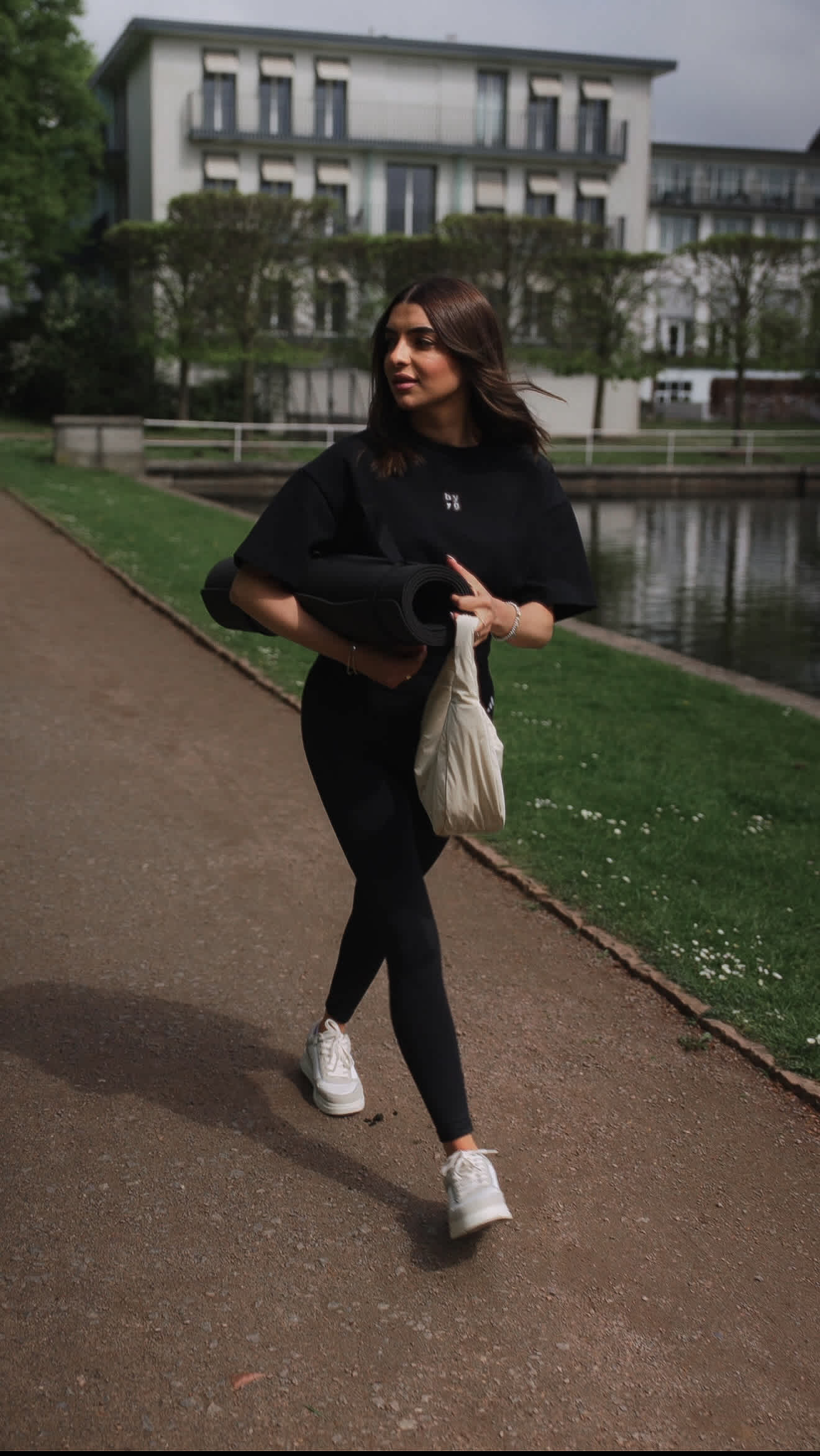 Junge Frau bei Spaziergang in schwarzem Outfit, bestehend aus Leggings und passendem T-Shirt samt Tasche