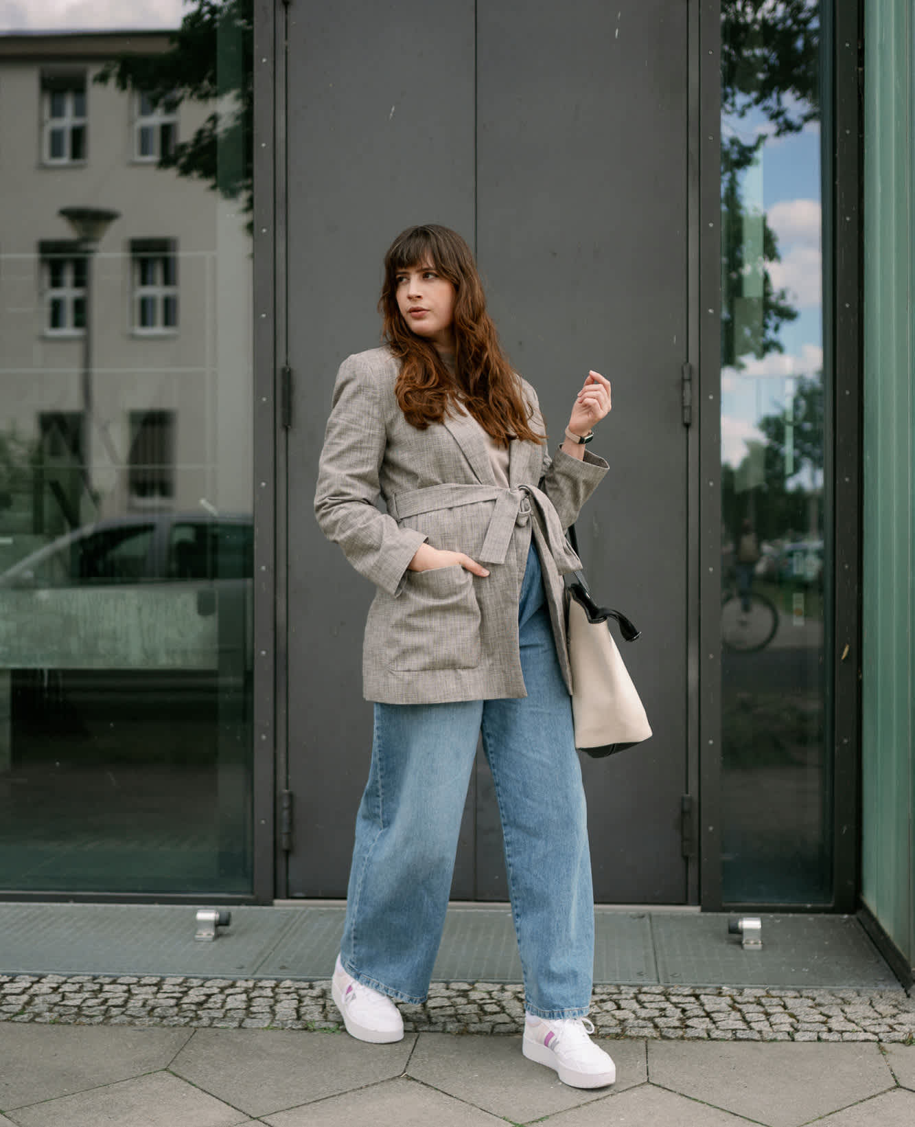 Frau in Business Chic-Outfit, trägt grauen Blazer und Wide Leg Jeans