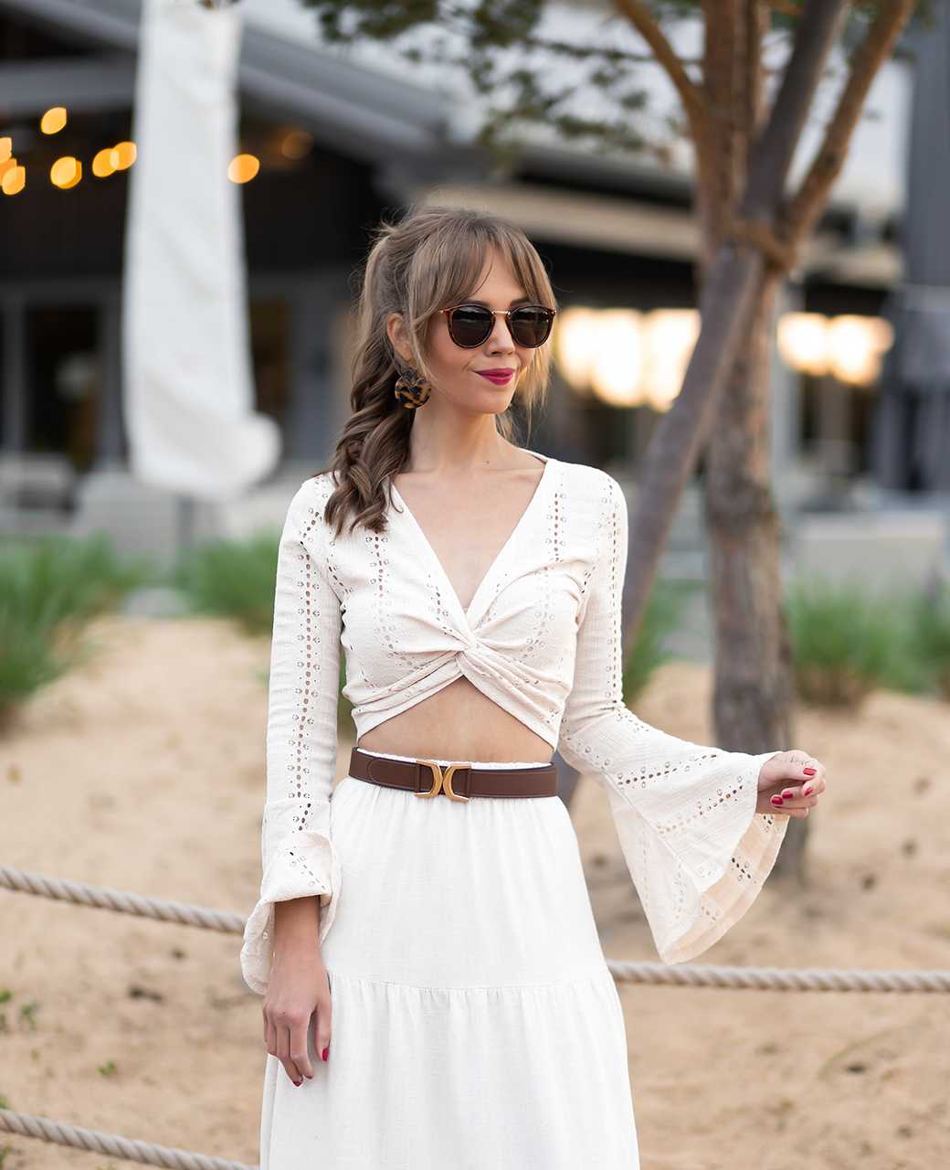 Frau mit langem Haar, trägt schwarze Sonnenbrille zu weißer Bluse mit Boho-Vibes