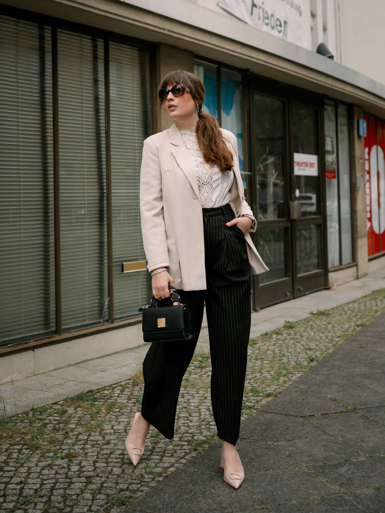 Frau in lässigem Business-Outfit, mit schwarzer Handtasche, stehend vor Gebäude