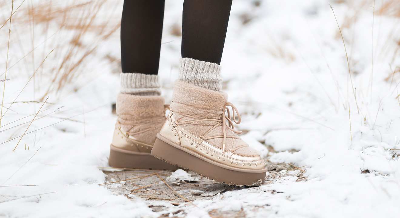 Nahaufnahme einer Person mit beigen Teddystoff-Boots in Winterlandschaft