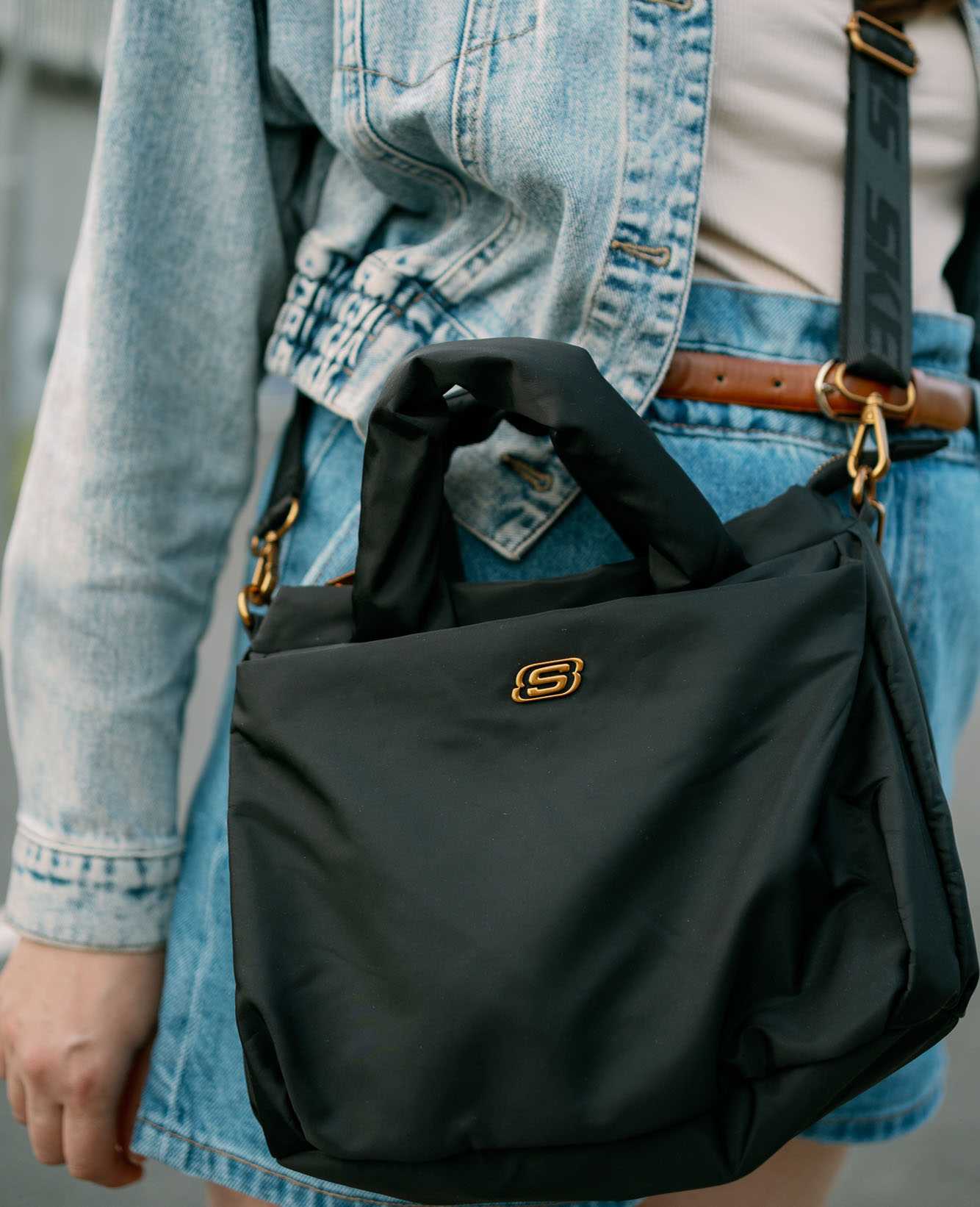 Frau in Jeans-Outfit trägt schwarze Umhängetasche mit Skechers-Logo