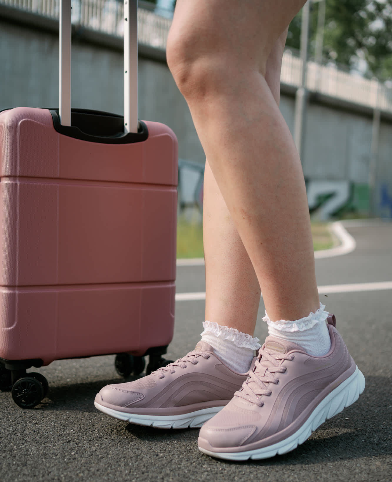 Frau in rosa Sneakern steht neben rosa Hartschalenkoffer