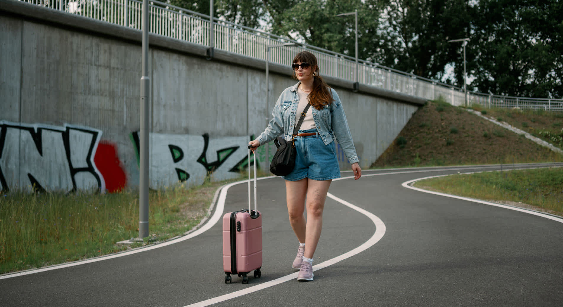 Frau in Jeans-Outfit spaziert mit Trolley über Straße