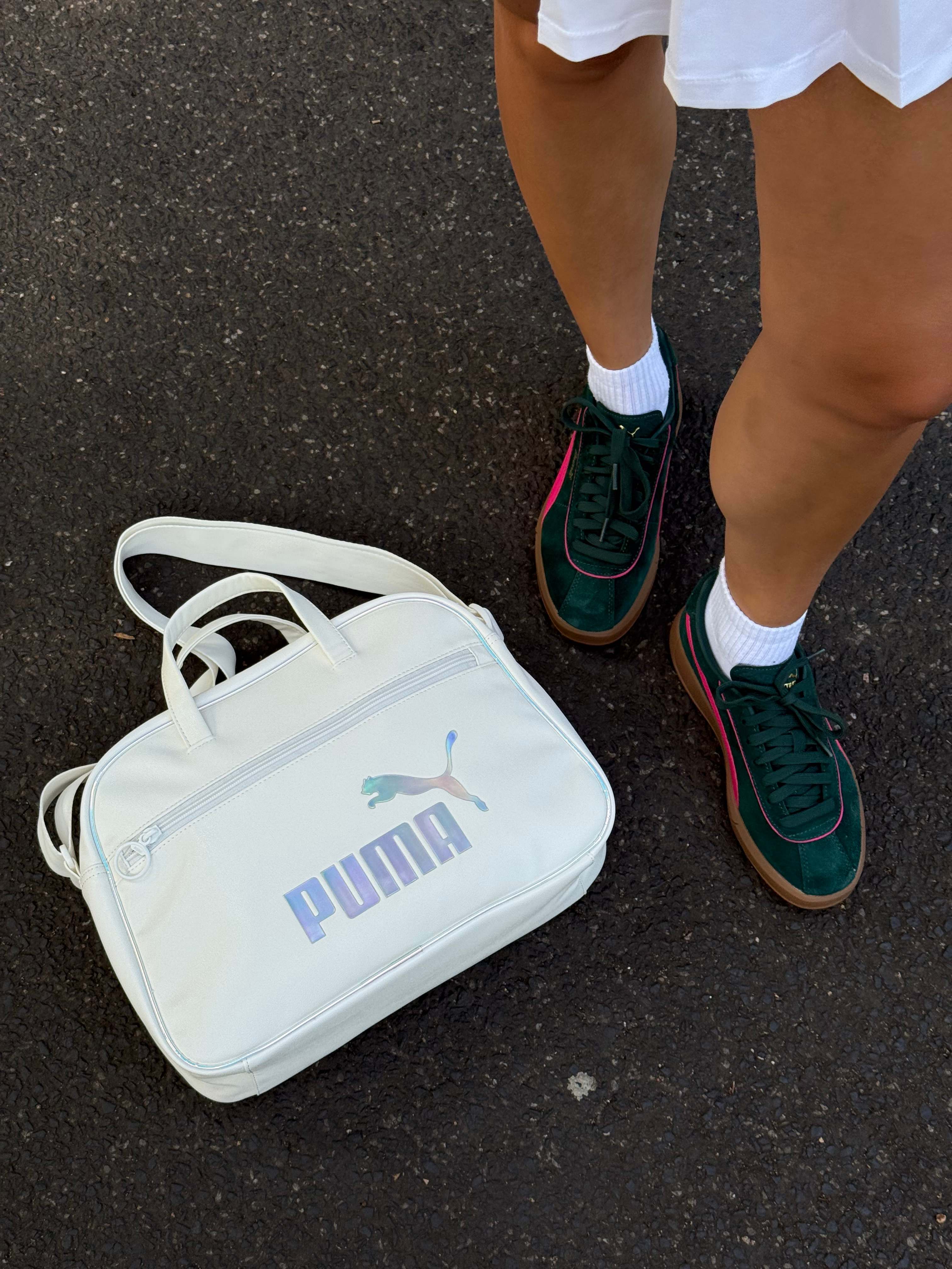 Frau in weißem Rock und Sneakern steht neben weißer Puma-Handtasche