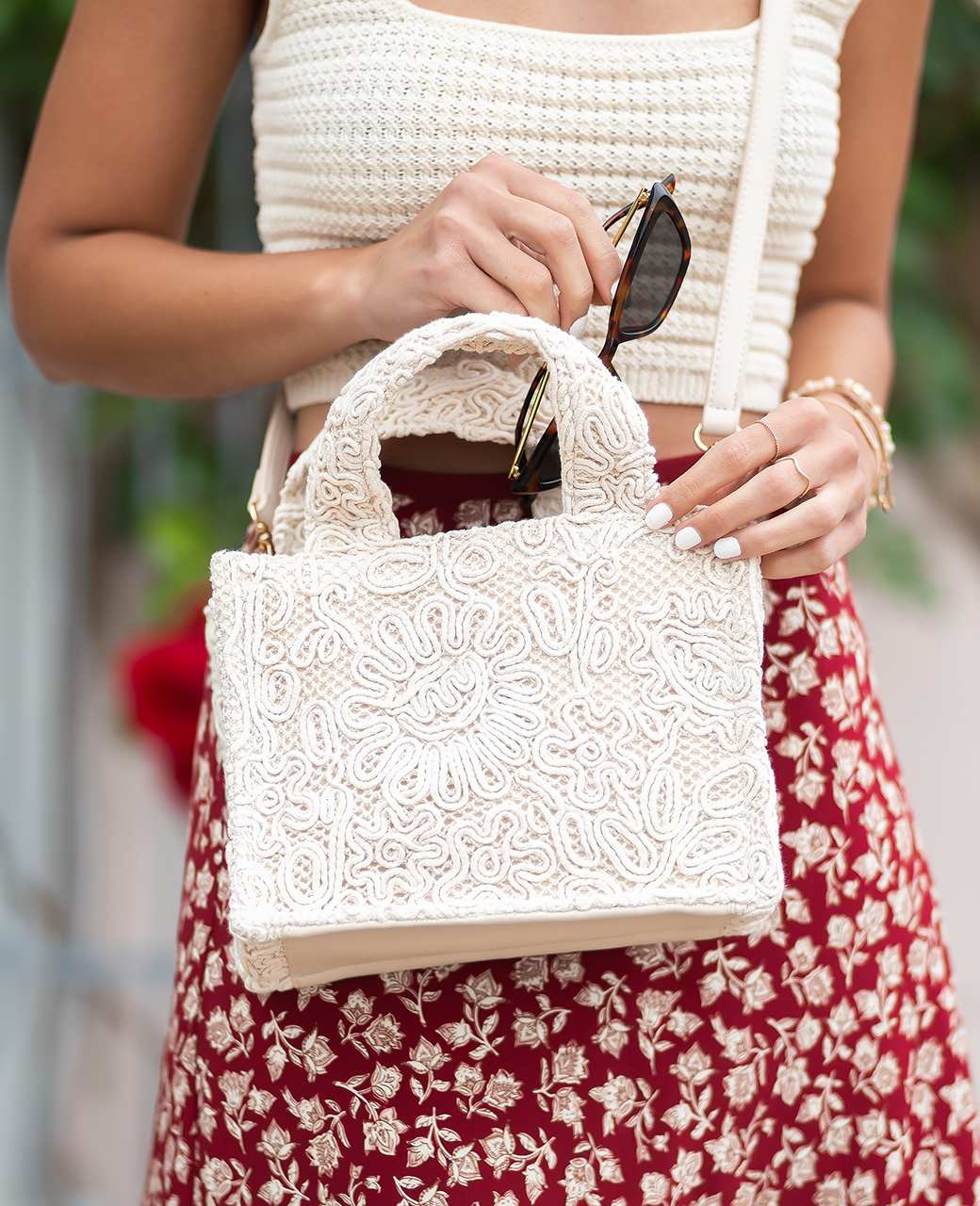 Frau holt schwarze Sonnenbrille aus ihrer weißen Handtasche im Boho-Style