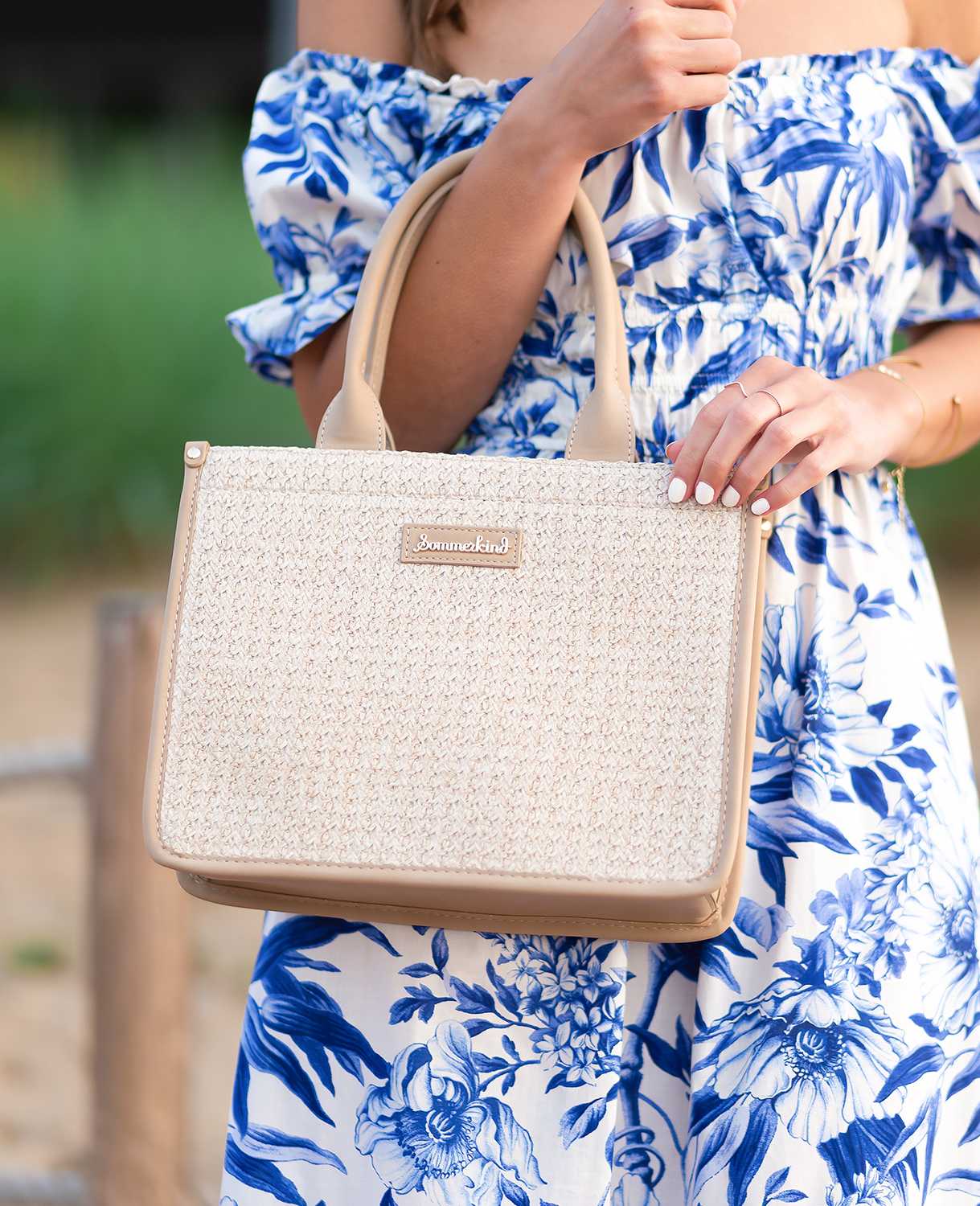 Frau in gemustertem Sommerkleid trägt Handtasche mit Bast-Details