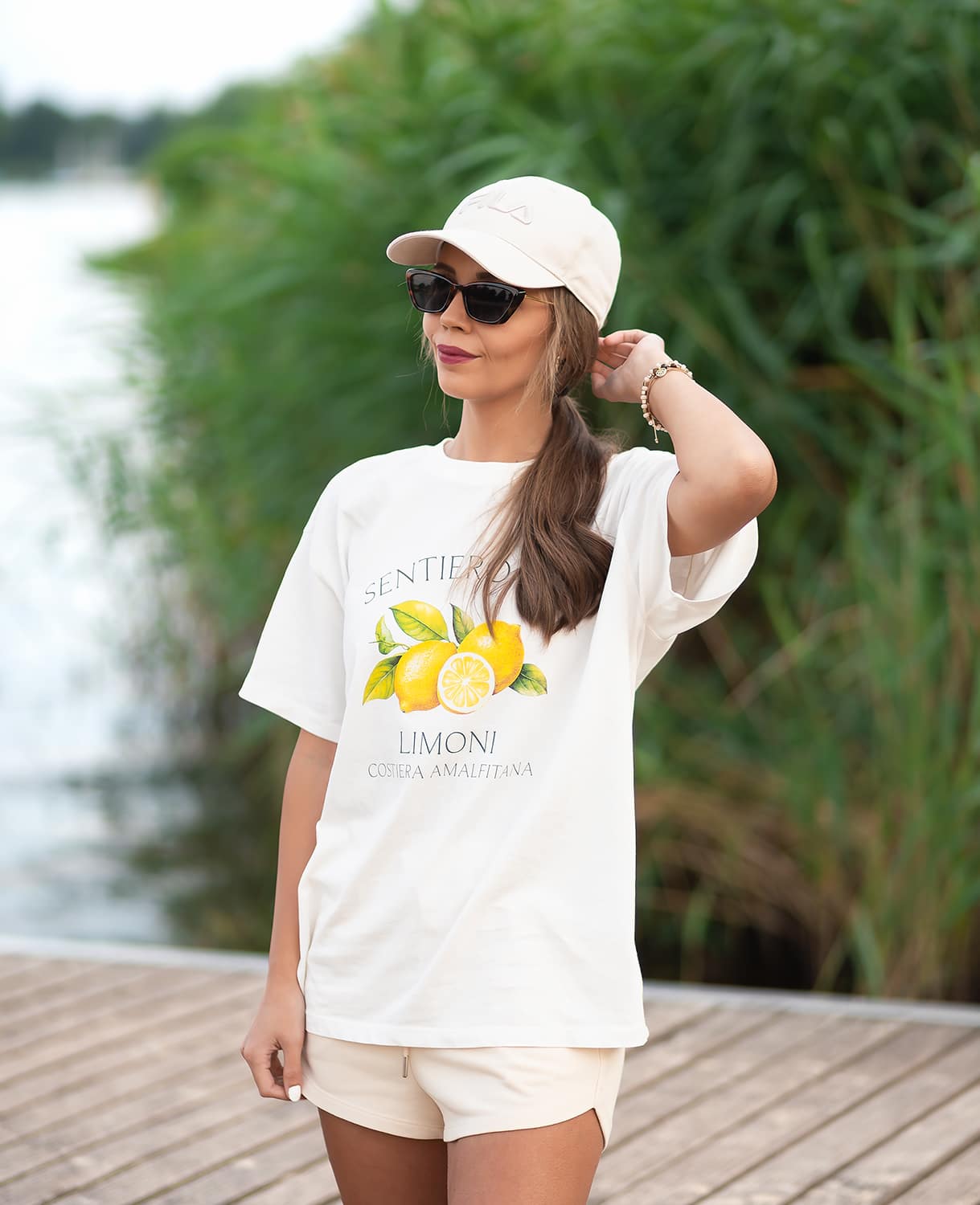 Frau steht auf Steg, gekleidet in lässiges Beach Style-Shirt mit passender weißer Kappe