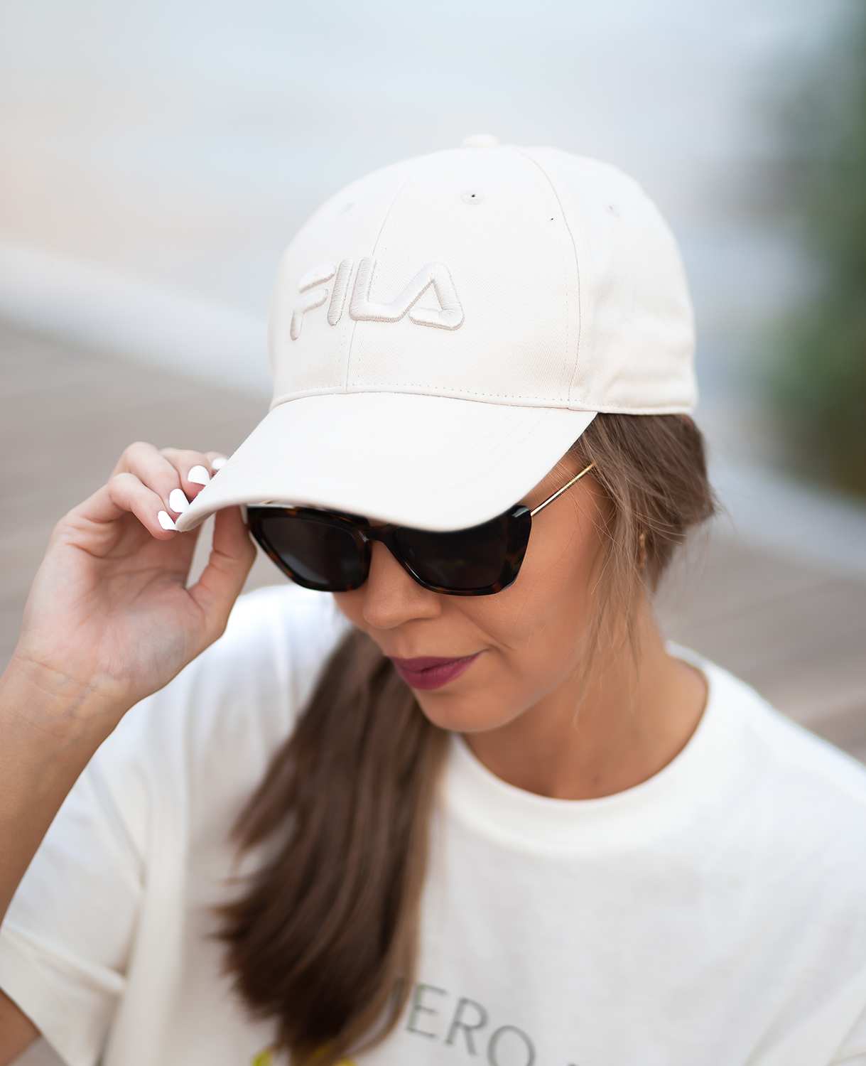 Frau trägt sportliches Strandoutfit, bestehend aus weißem Shirt mit Kappe und schwarzer Sonnenbrille