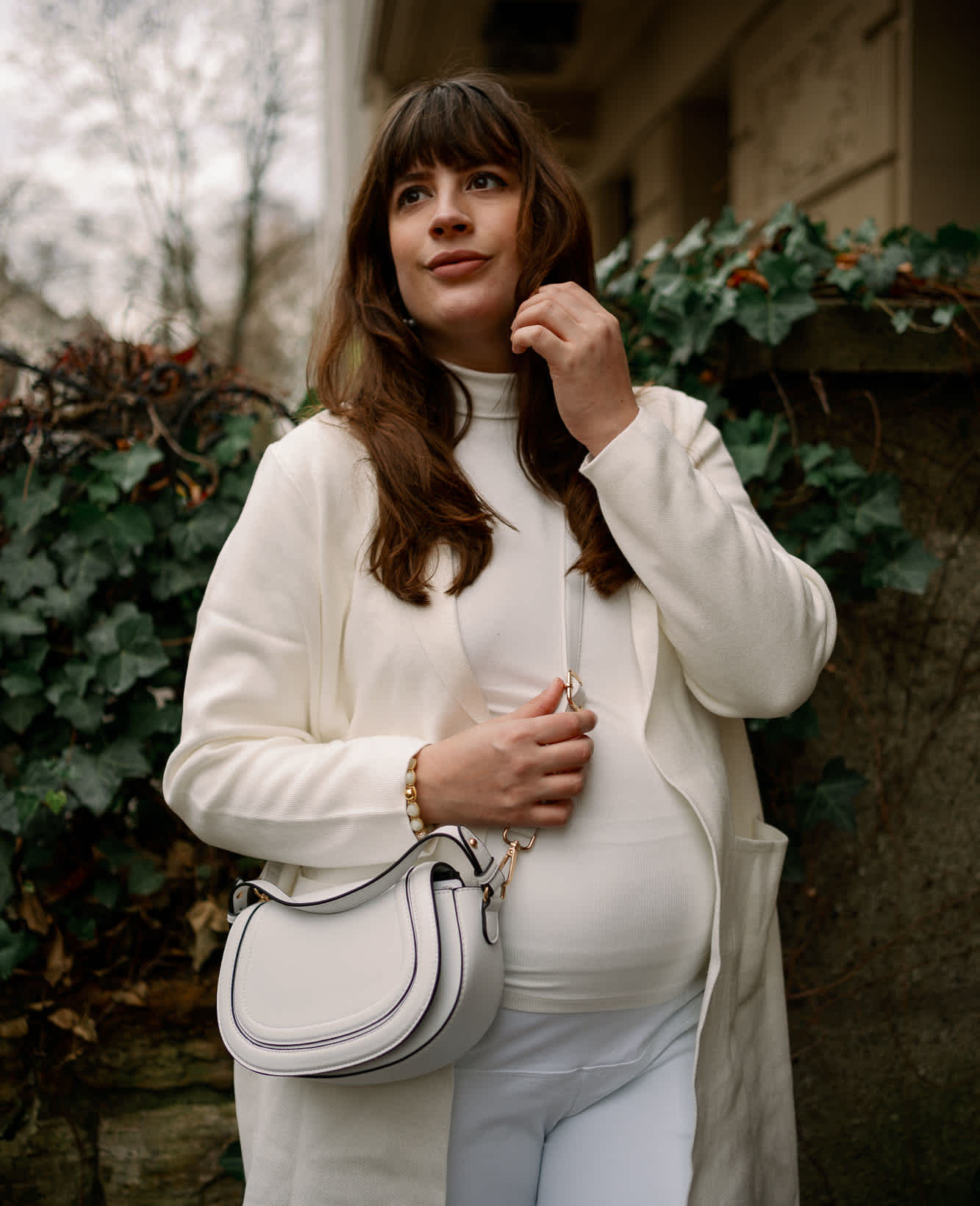 Frau posiert in einem All White Outfit, stehend vor einem Busch