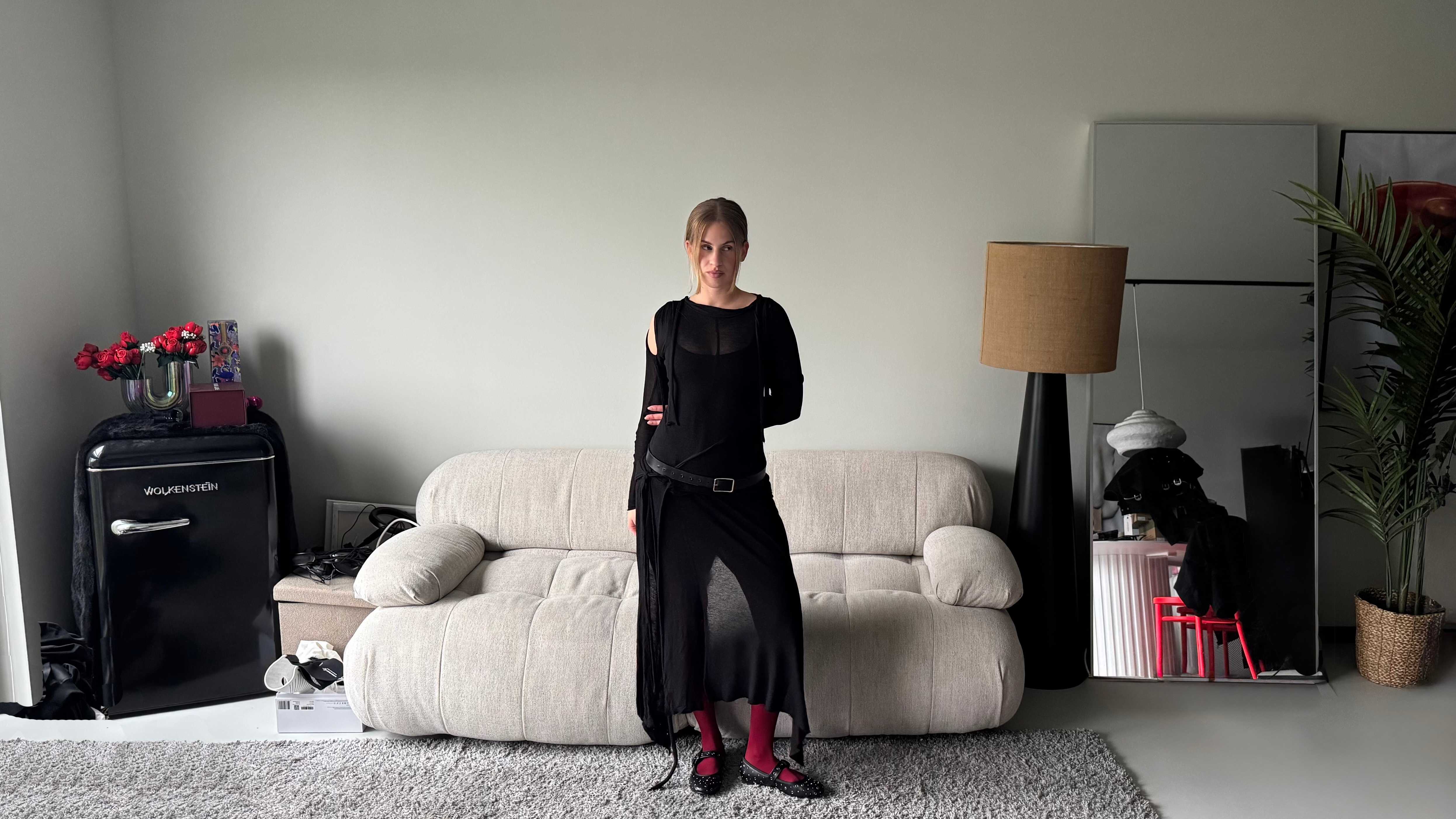 Frau in tiefschwarzem Balletcore-Outfit steht in Wohnzimmer-Umgebung
