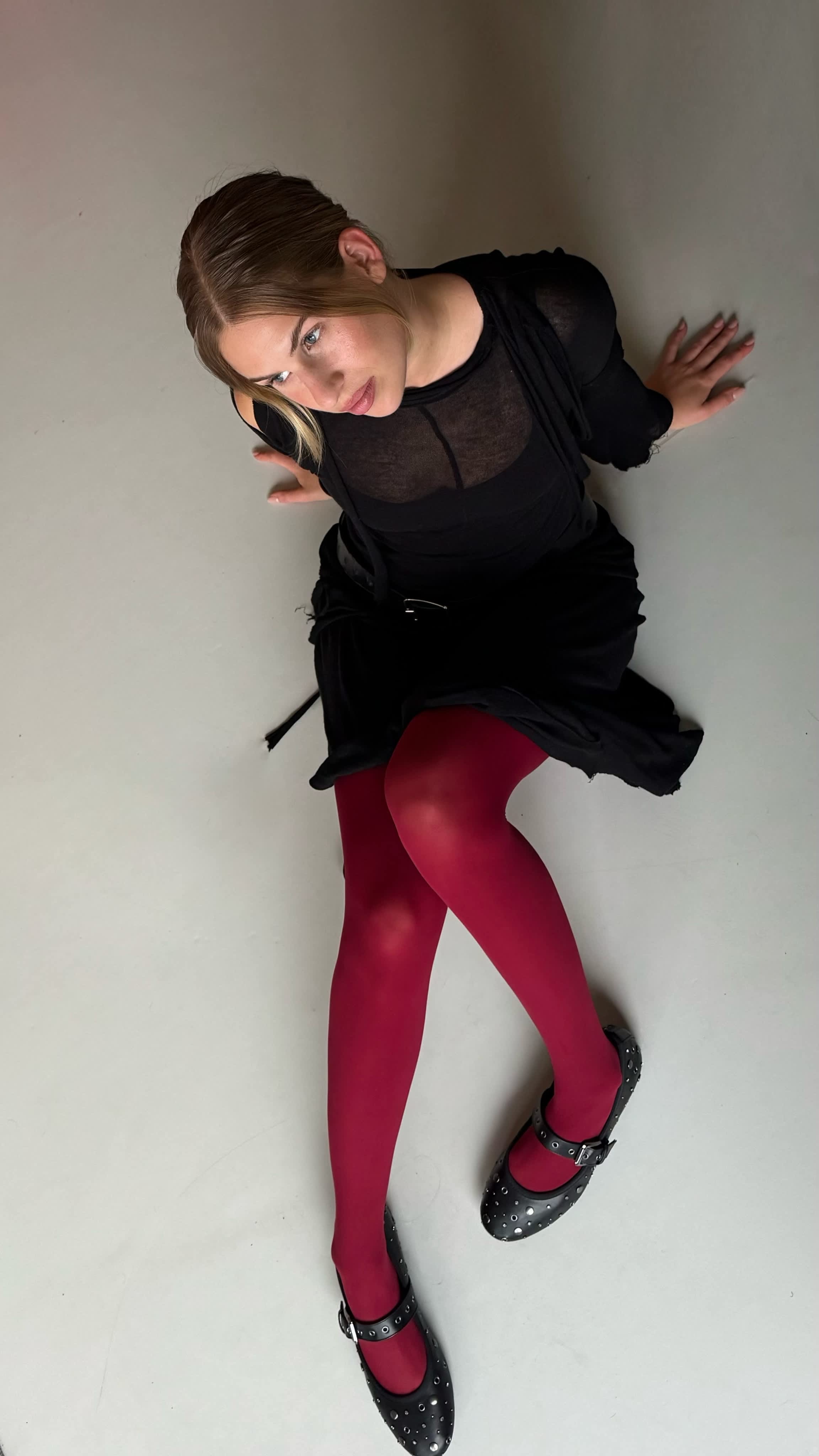 Frau in schwarzem Outfit und roter Strumpfhose sitzt auf Teppich, Ansicht von oben
