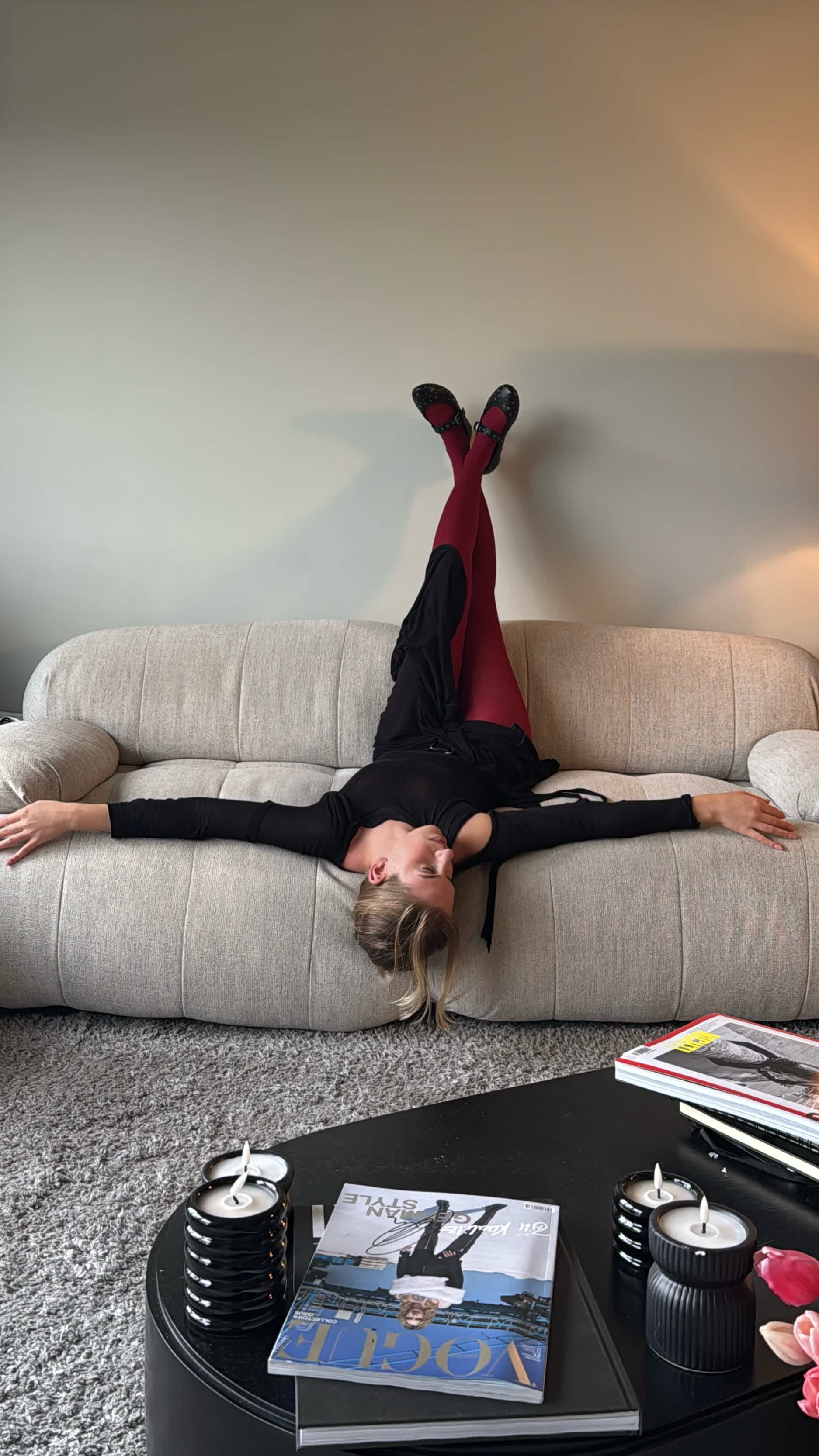 Frau in schwarzem Balletcore-Outfit liegt kopfüber auf grauer Couch