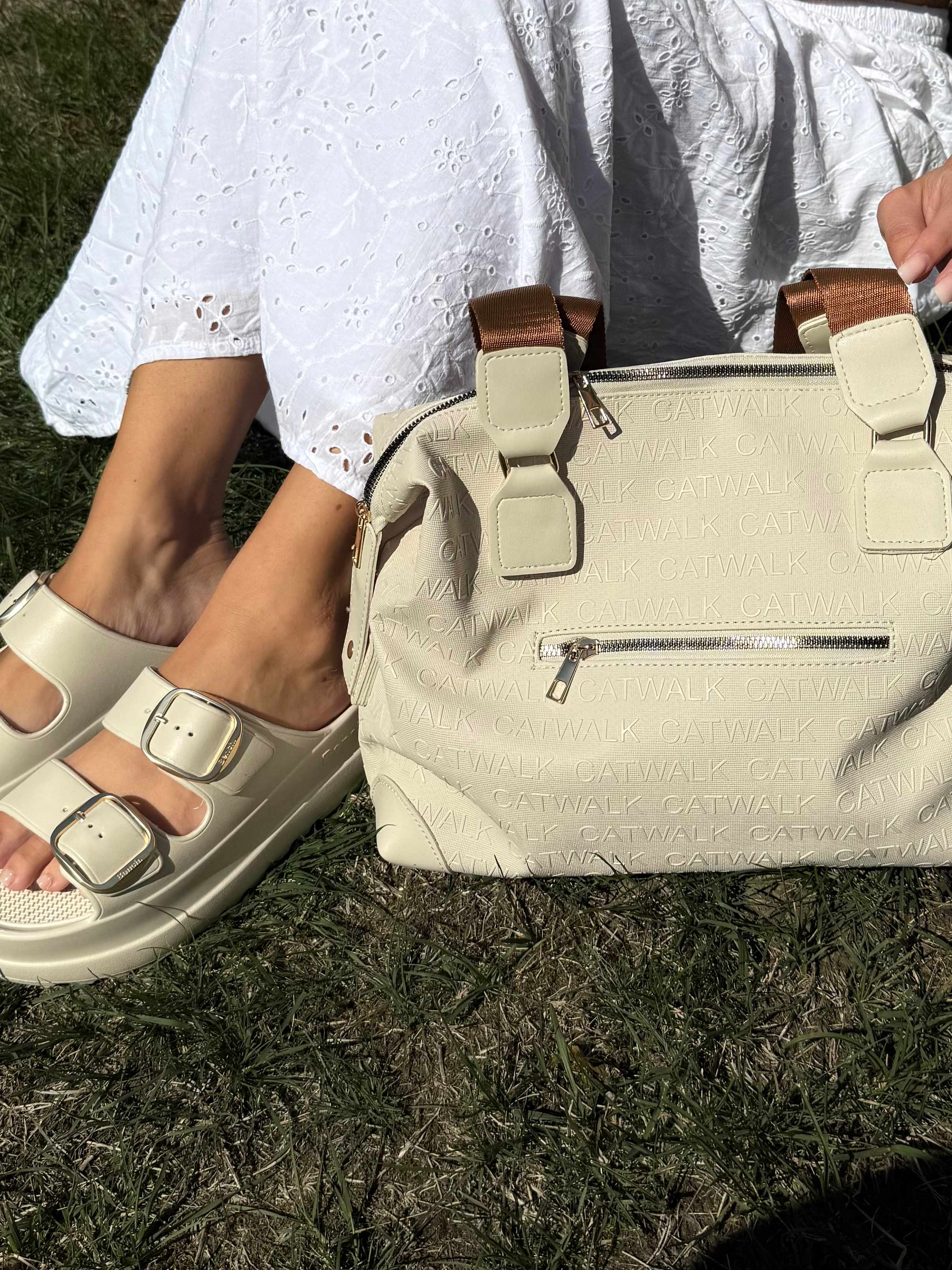 Close-Up einer Frau in weißem Kleid, mit klobigen Sandalen und Handtasche, auf Rasen sitzend