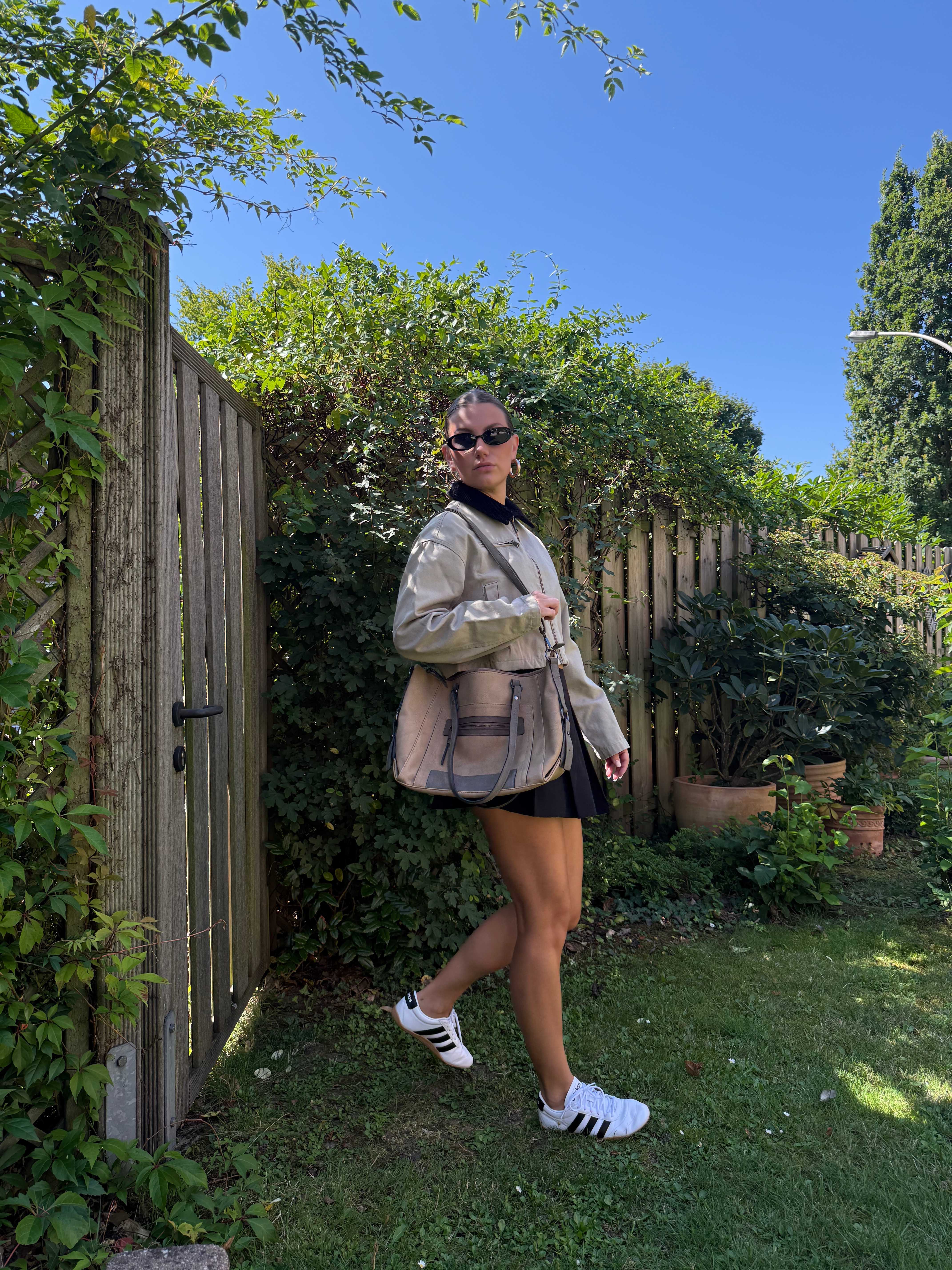 Frau posiert in schwarz-grauem Gartenparty-Outfit im Garten
