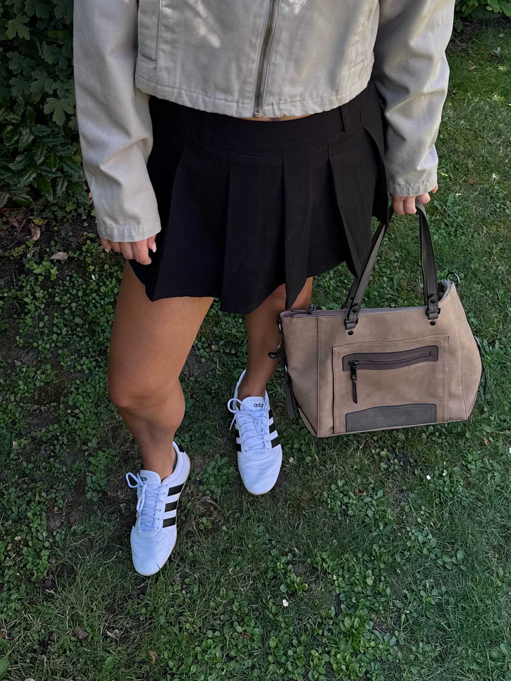 Frau steht auf Rasen, trägt weiiße Sneaker und schwarzen Rock, mit Handtasche in der Hand, Top-Down-Ansicht