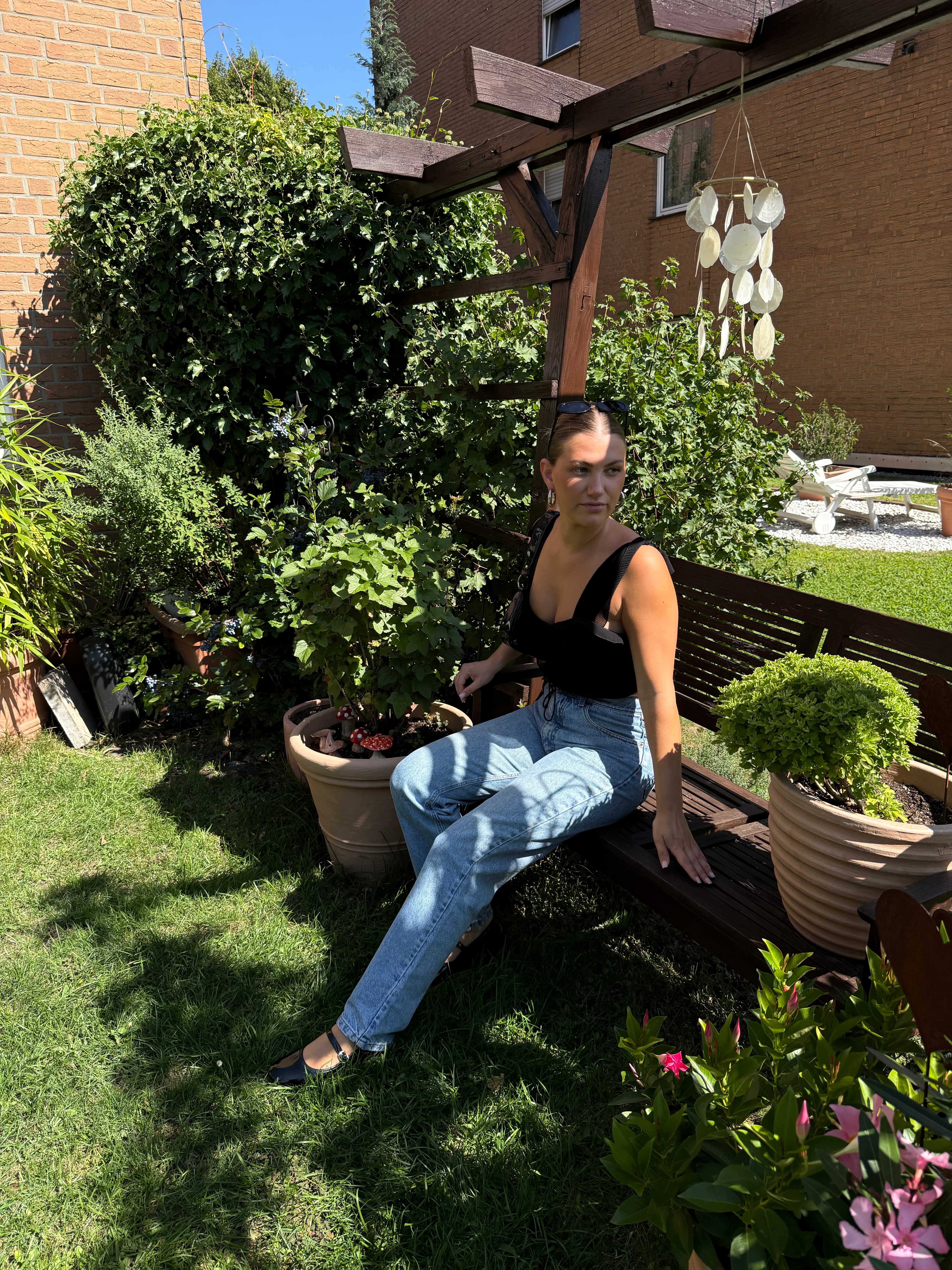 Frau in schwarzem Top und Jeanshose sitzt auf Holzbank im Garten