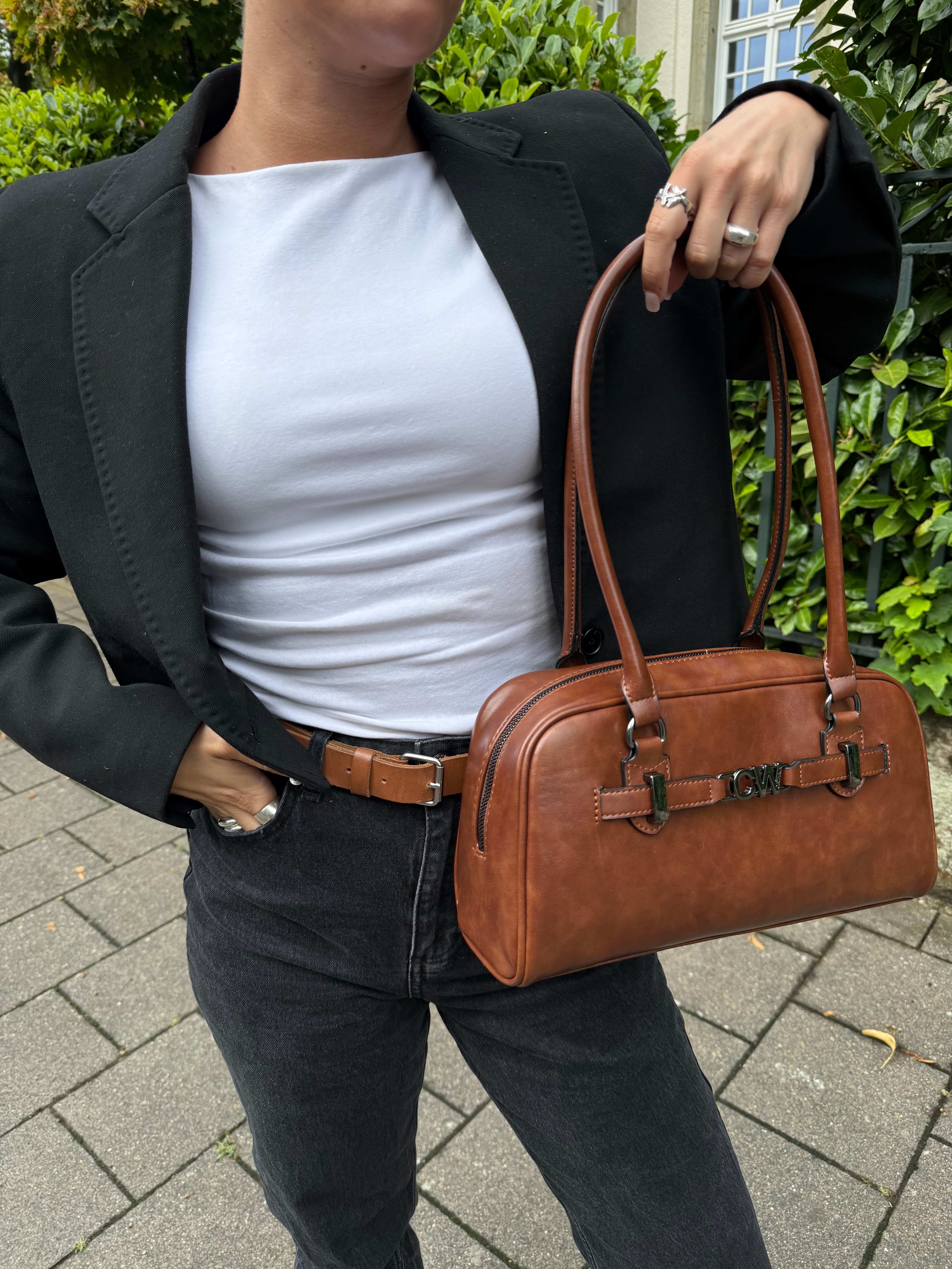 Frau in dunkelblauem Blazer und weißem Shirt präsentiert ihre braune Handtasche
