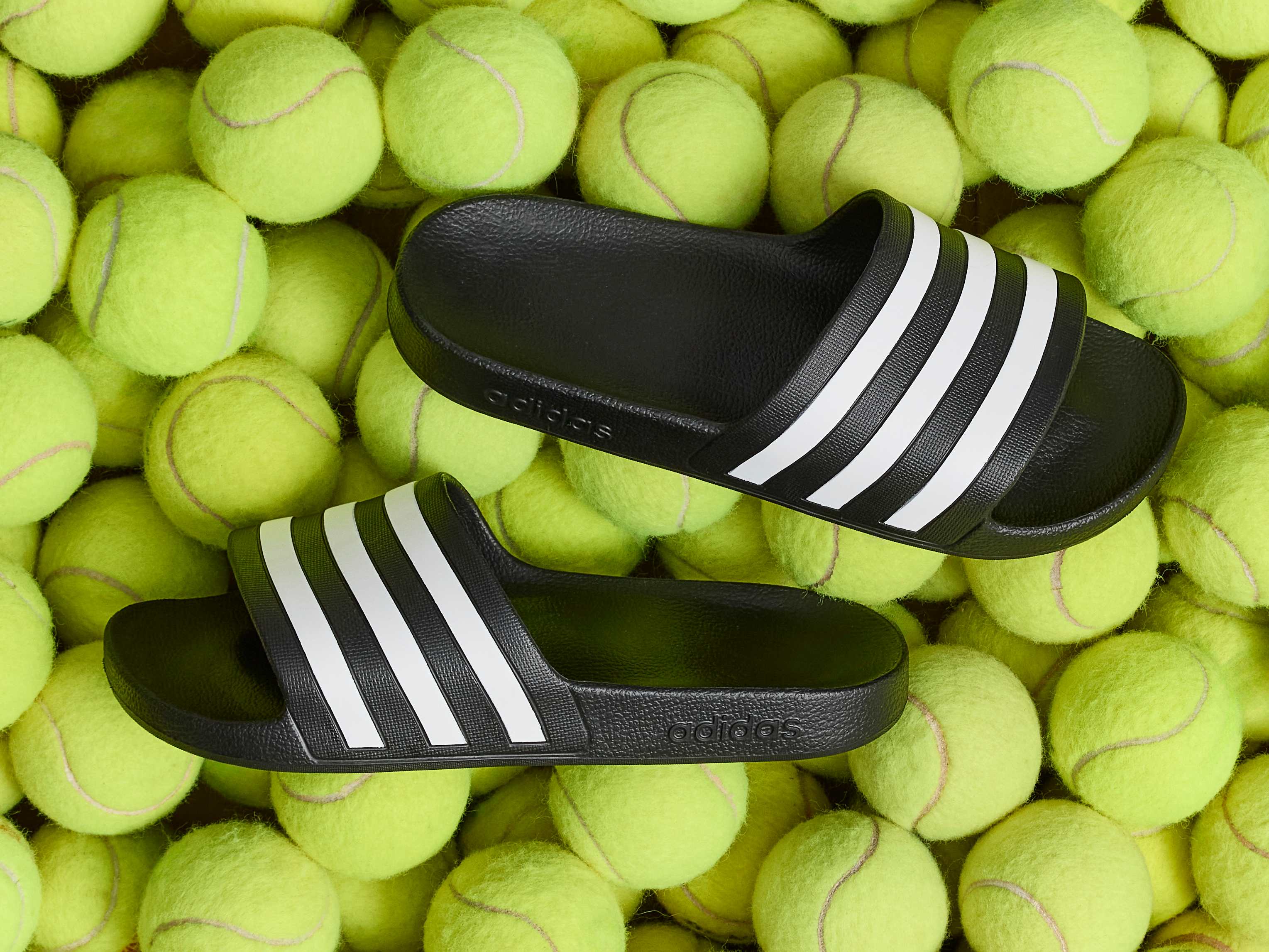 Schwarze Adidas-Badeschlappen inmitten einer Masse an Tennisbällen