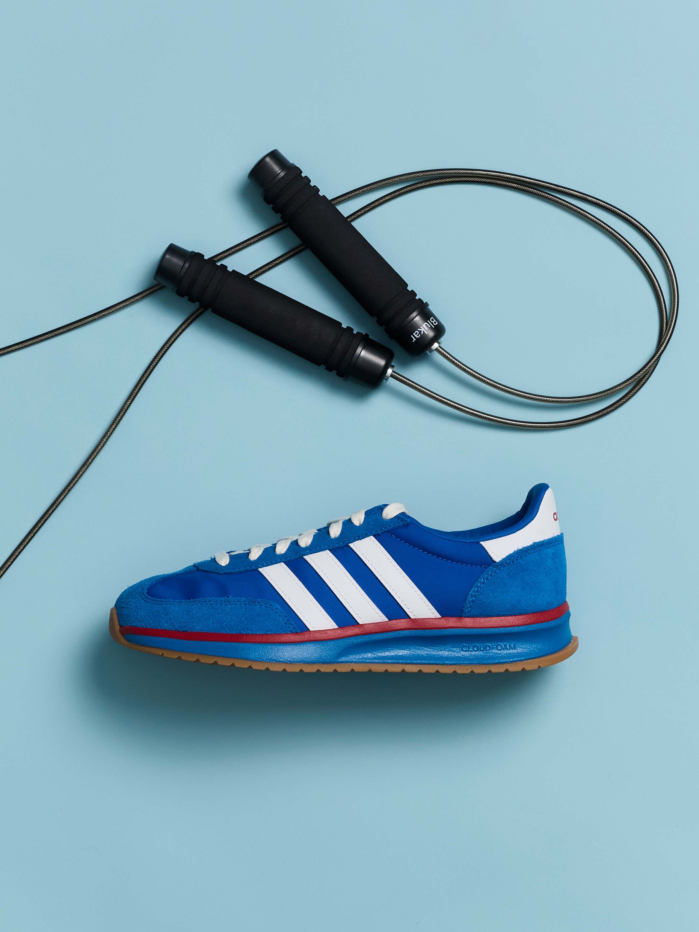 Blauer Adidas-Sportsneaker liegt unter einem schwarzen Springseil