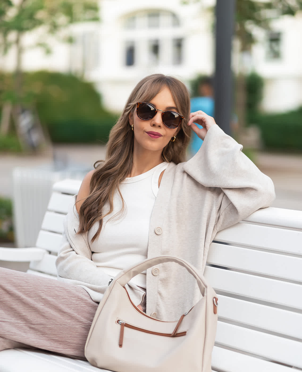 Junge Dame in weißem Outfit, mit Sonnenbrille, sitzt entspannt auf Parkbank