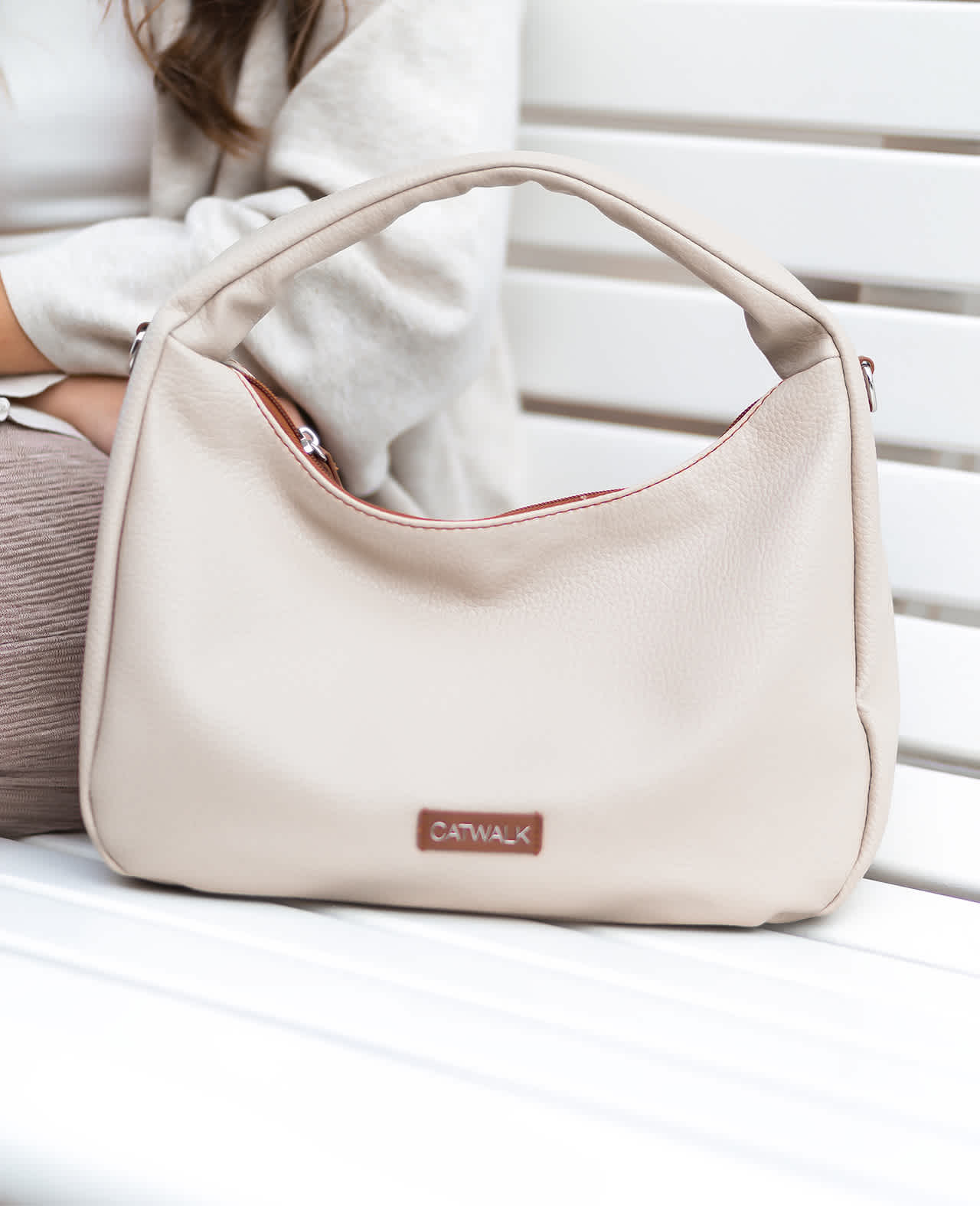 Weiße Catwalk-Tasche steht auf weißer Parkbank, Frau sitzt daneben