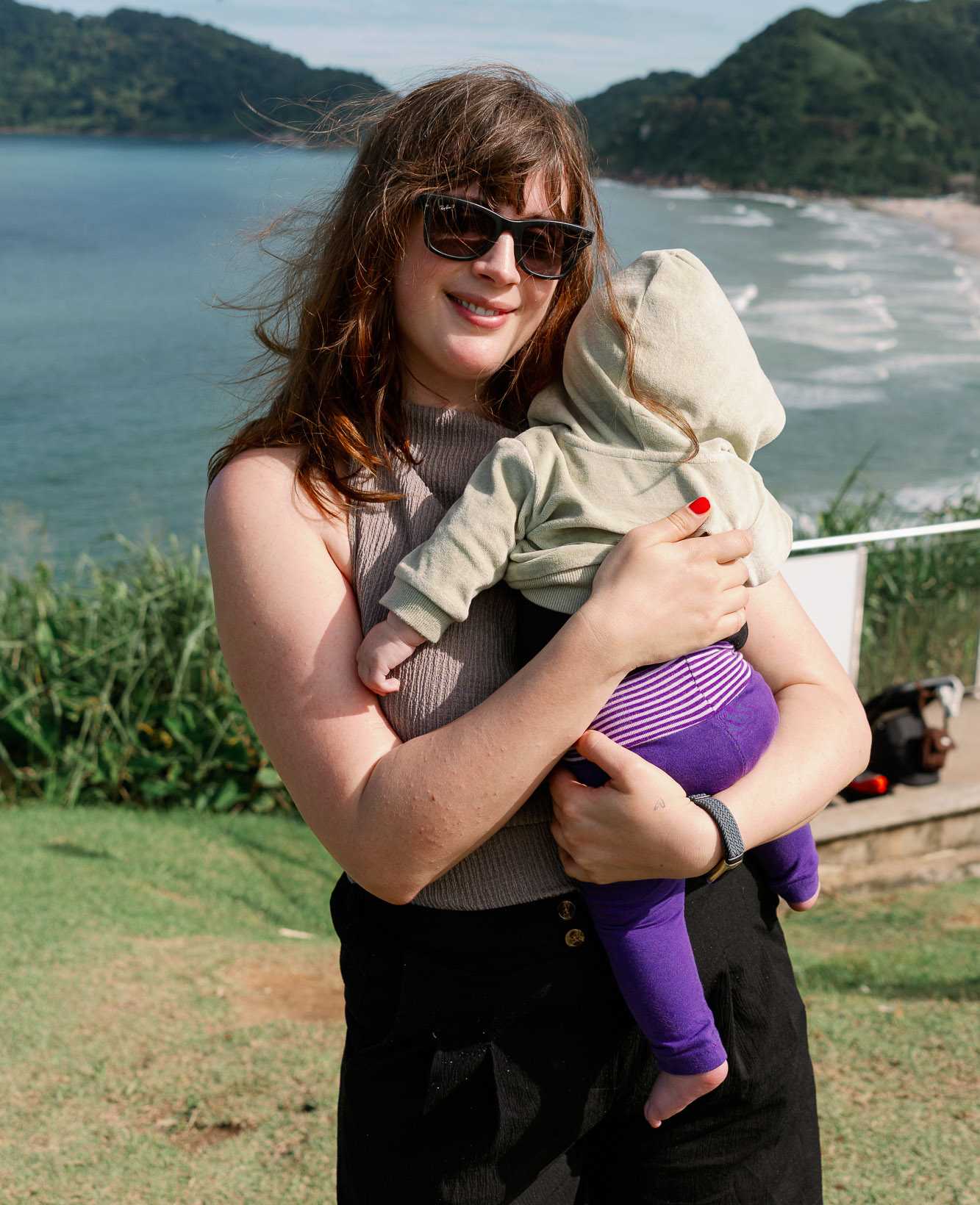 Frau mit Sonnenbrille hält Baby auf dem Arm, mit See im Hintergrund