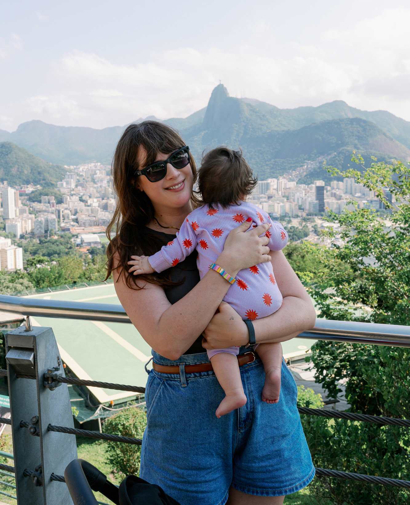 Frau in schwarzem Top und Jeans-Shorts, hält Baby im Arm, steht an Aussichtspunkt