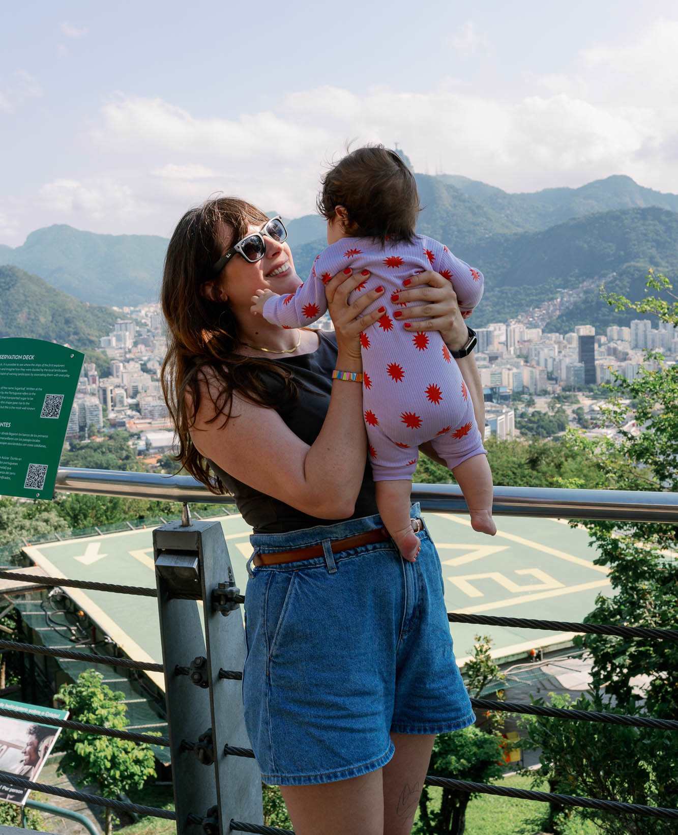 Frau hält Baby hoch, mit brasilianischer Stadtkulisse im Hintergrund