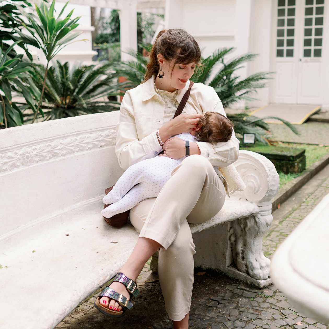 Frau hält Baby im Arm, sitzt auf weißer Steinbank