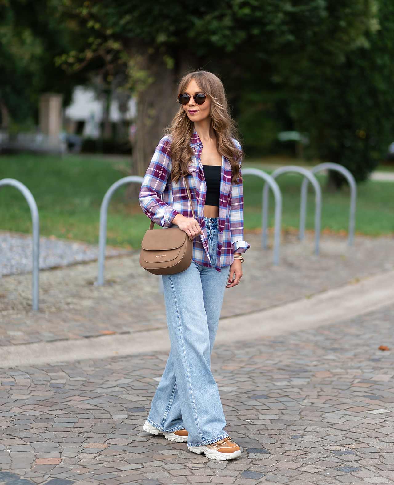 Frau in kariertem Hemd mit blauer Jeanshose, Chunky Sneakern und brauner Umhängetasche